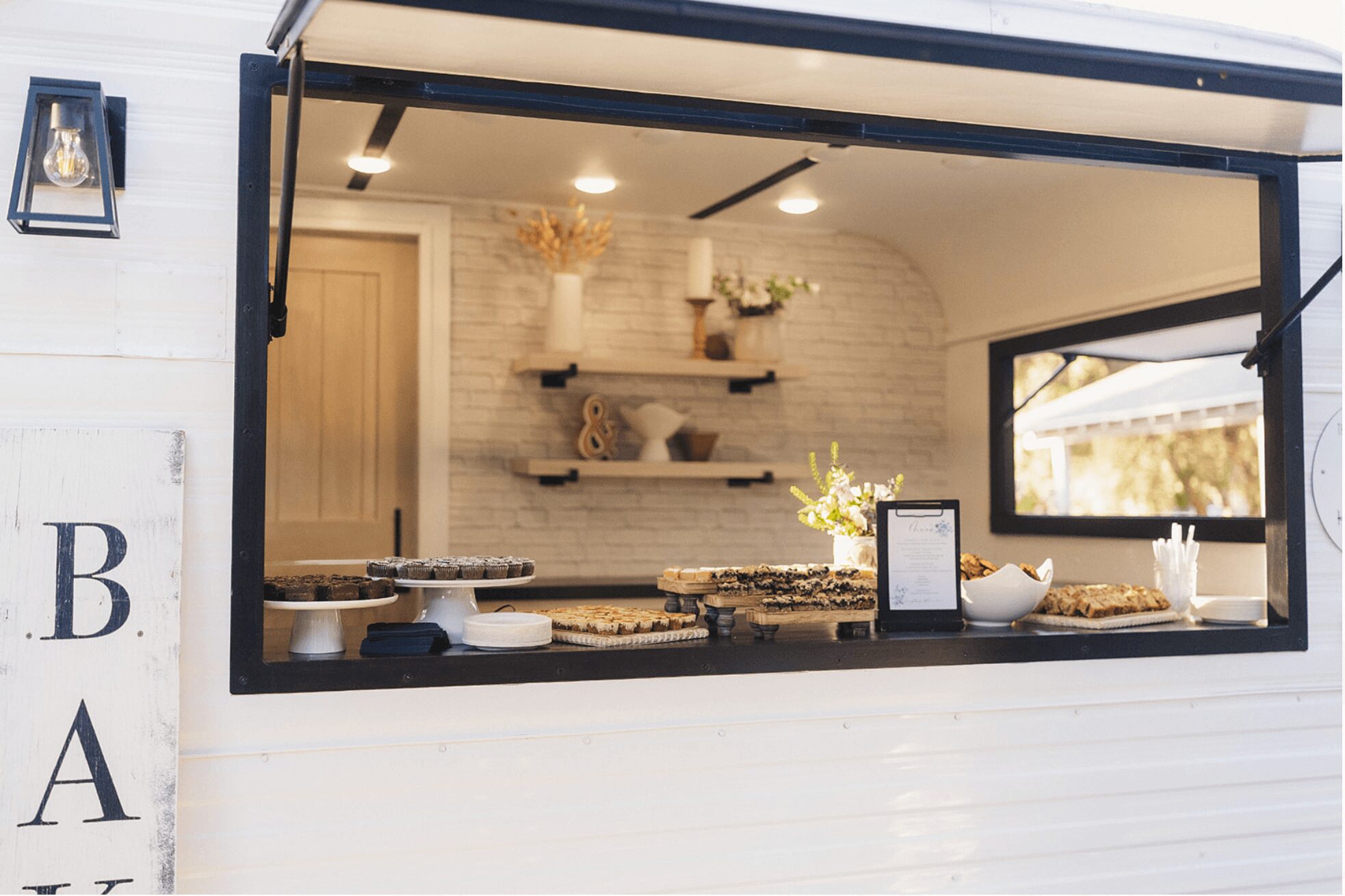 View of a food stand with a window displaying baked goods and a small interior shelf with decorations.
