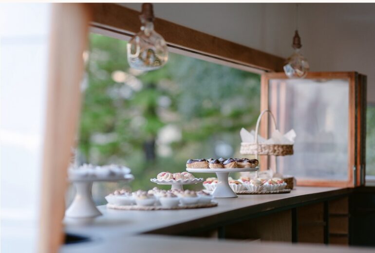 Display of cupcakes and desserts on a windowsill with a blurred outdoor background, in a cozy setting.