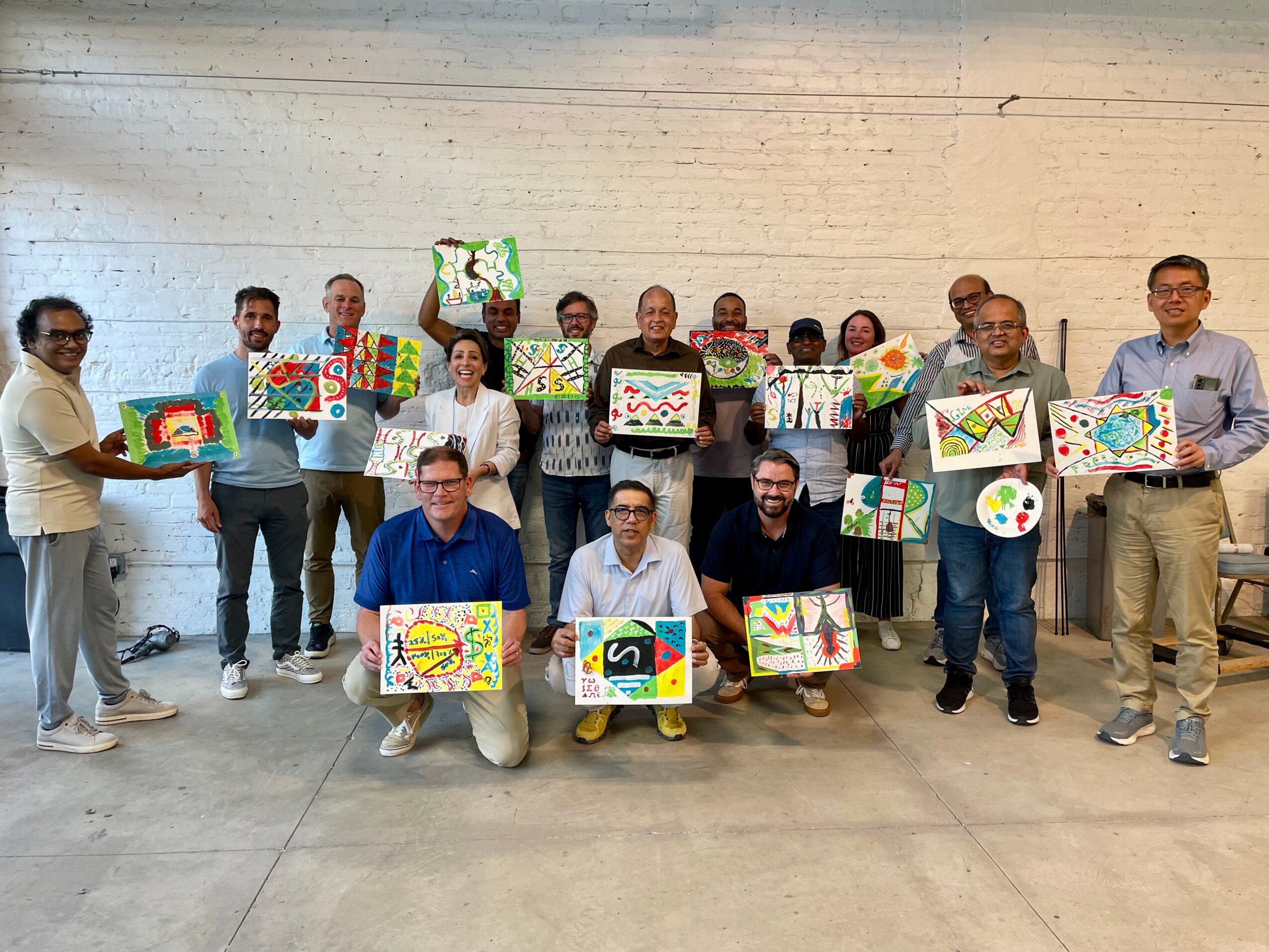 Group of people holding colorful artwork in a spacious room with a white brick wall.