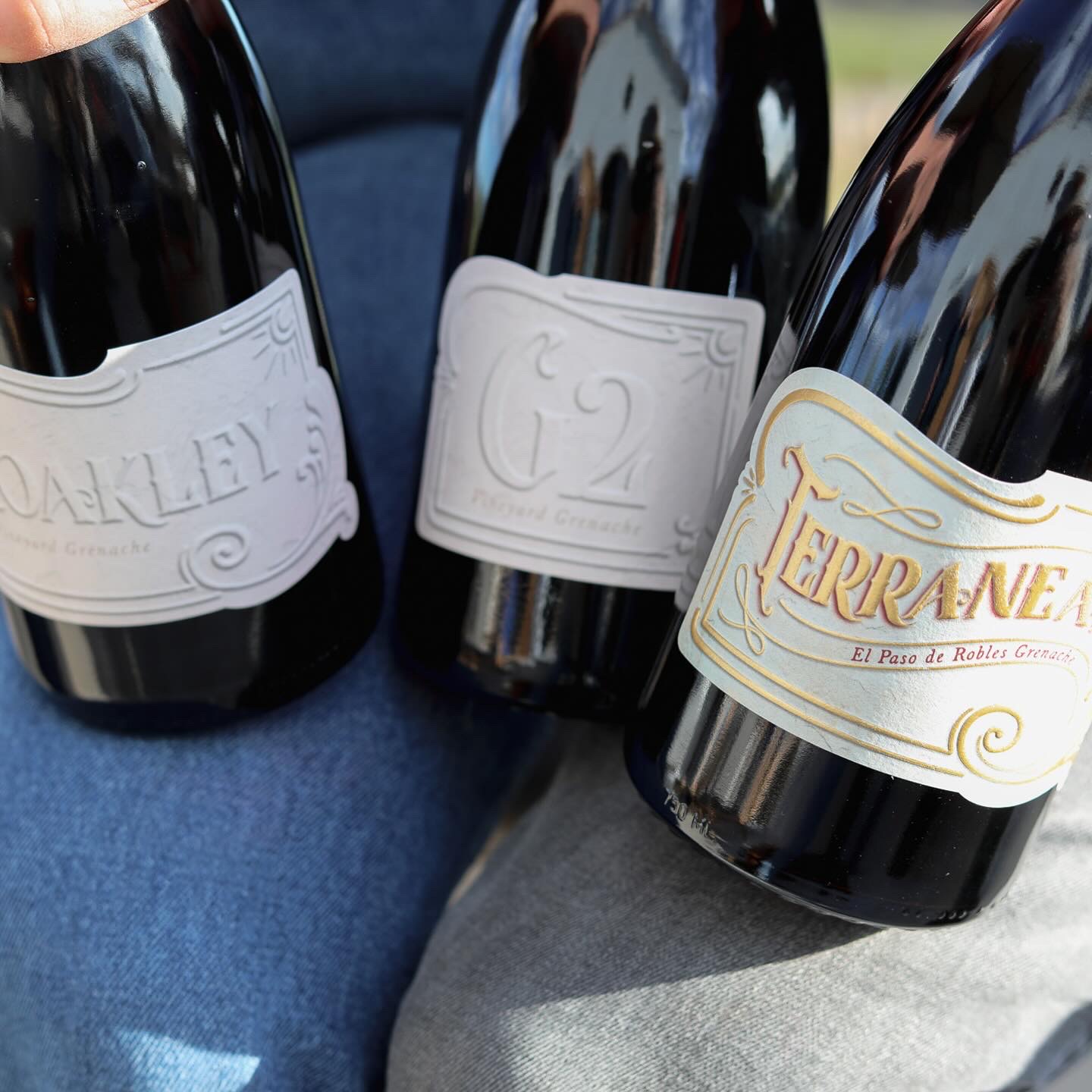 Three wine bottles with labels, held close together, with a blue and gray background.
