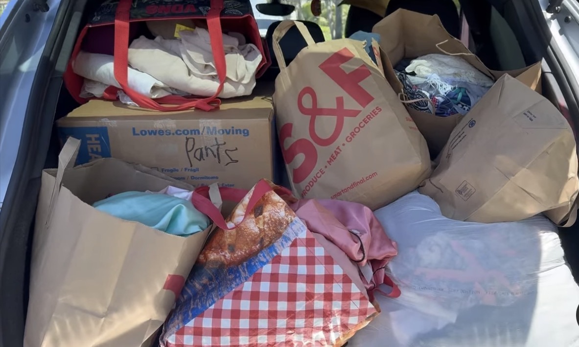 Car trunk filled with shopping bags, boxes, and clothing items, some with visible packaging and fabric.