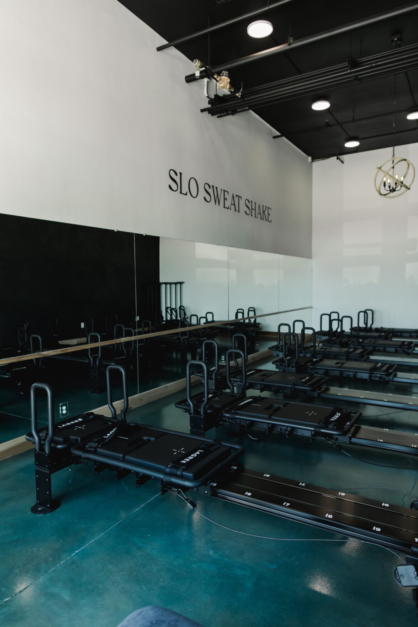 Indoor fitness studio with rowing machines, a mirror wall, and a sign reading 'SLO Sweat Shop.'