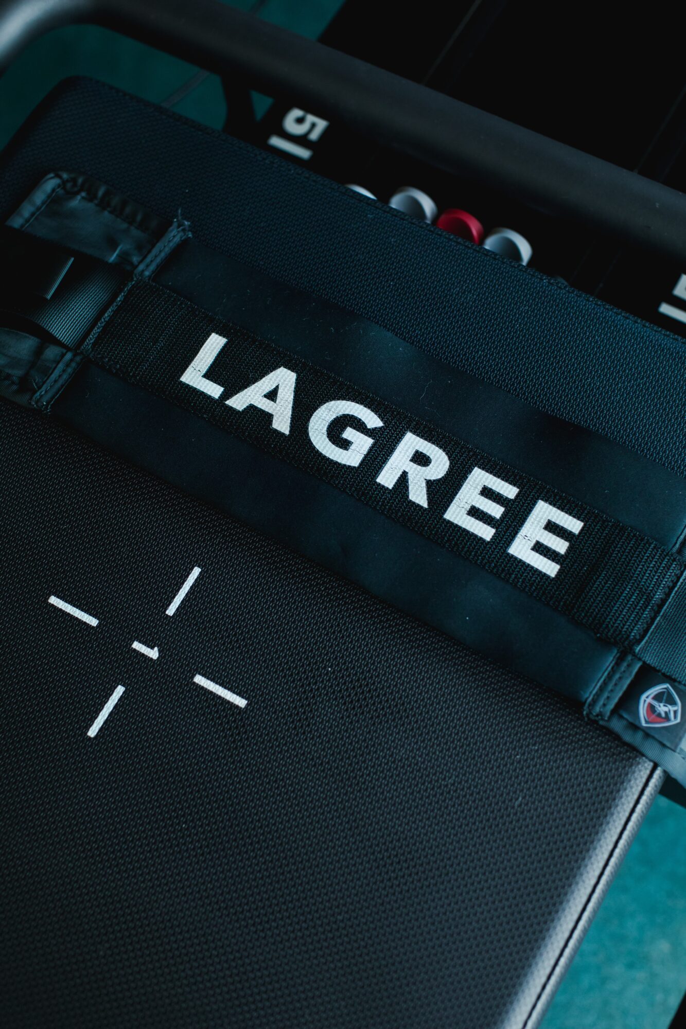 Close-up of a black bag with a strap labeled 'LAGREE' and a laptop surface visible.