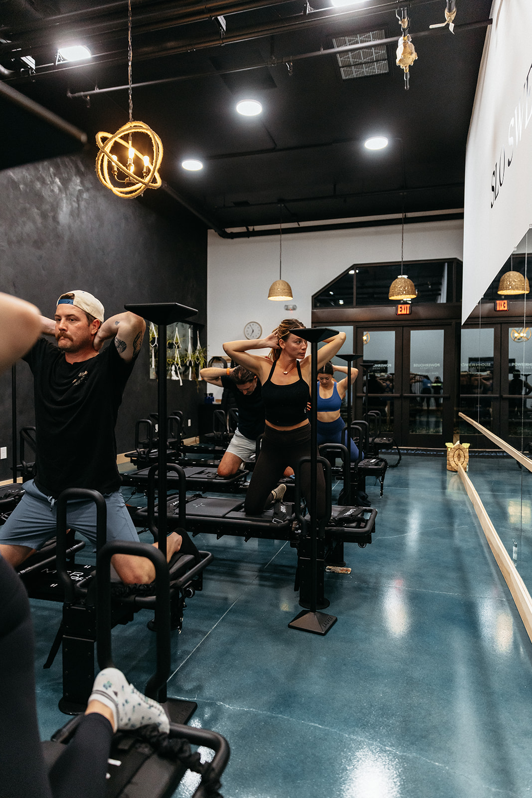 People working out in a gym with black walls, large windows, and modern lighting fixtures, including a spherical pendant light.