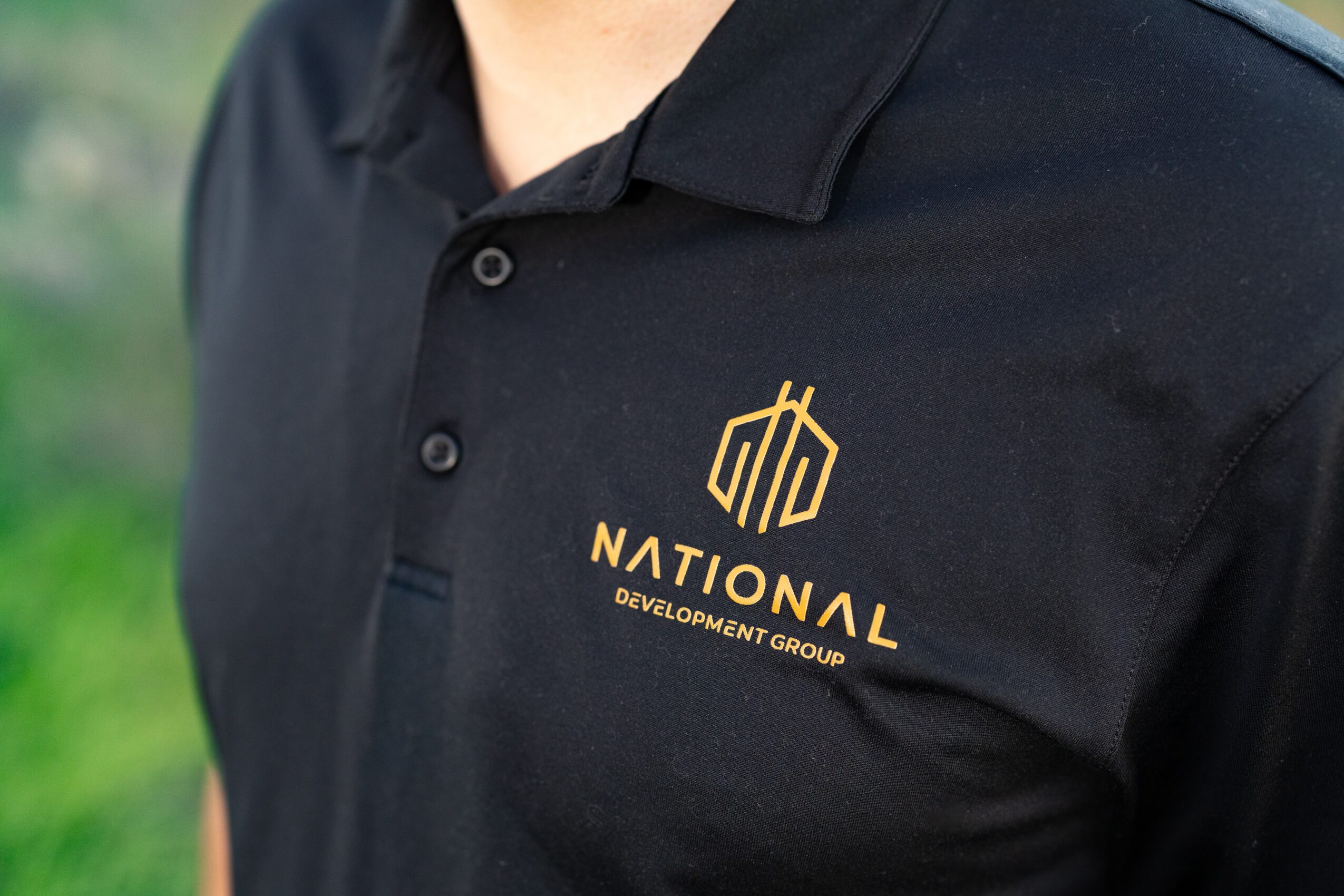 Close-up of a person wearing a black polo shirt with a gold logo and text on the chest.