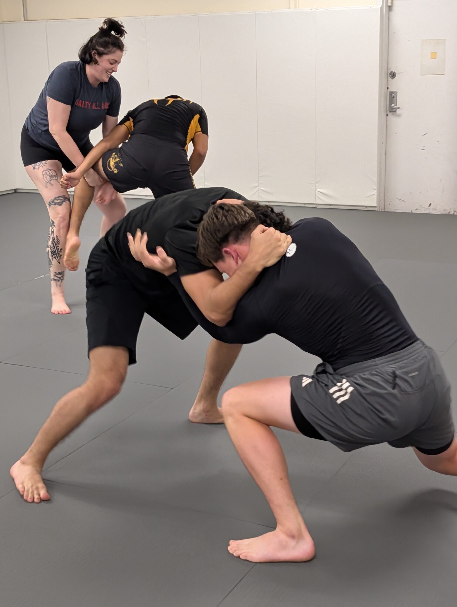 Two people grappling on the floor while two others observe in a gym setting.