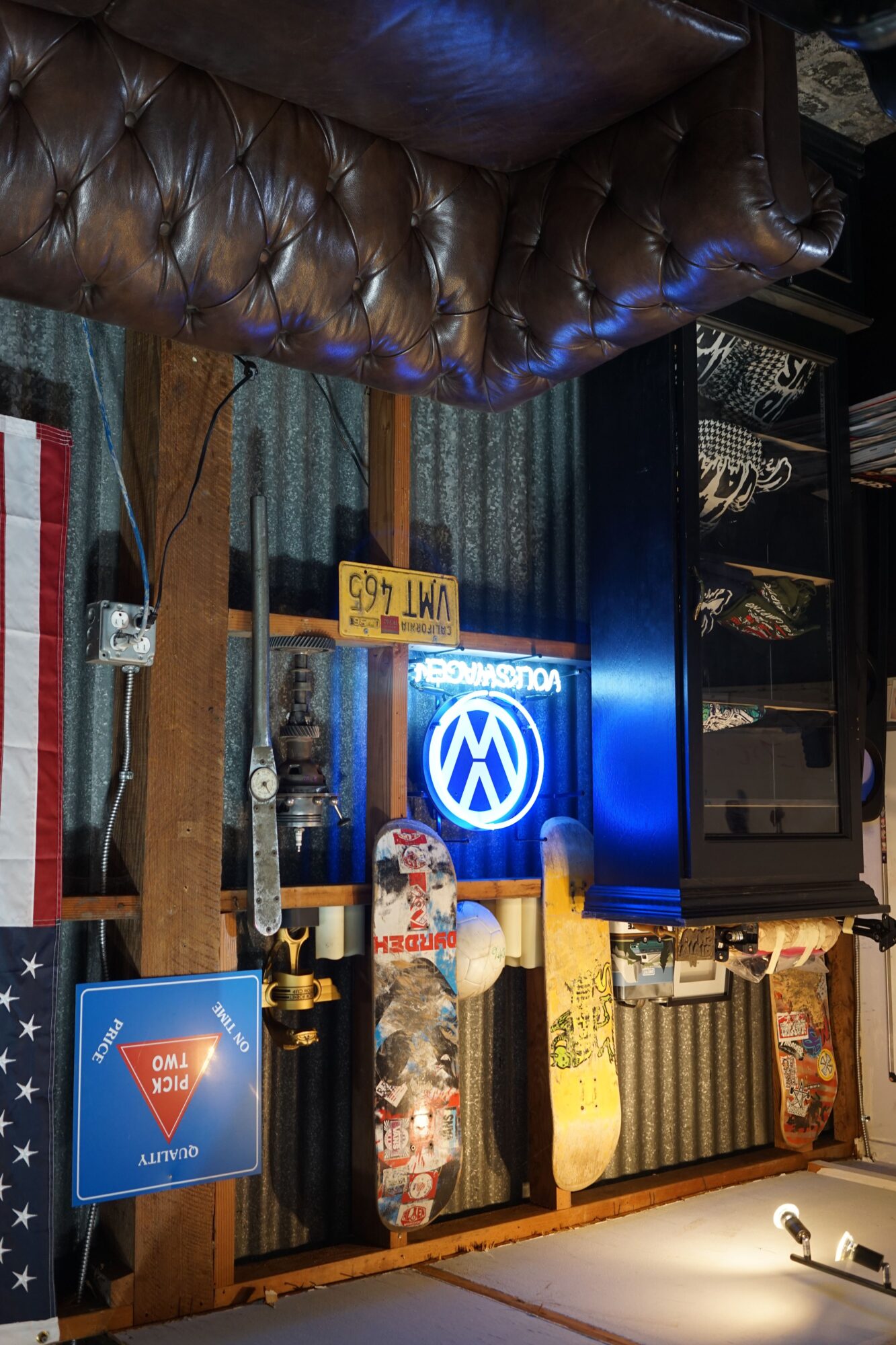 Bar with leather couch, illuminated Volkswagen logo, shelves with bottles, and a blue sign, viewed from the side.