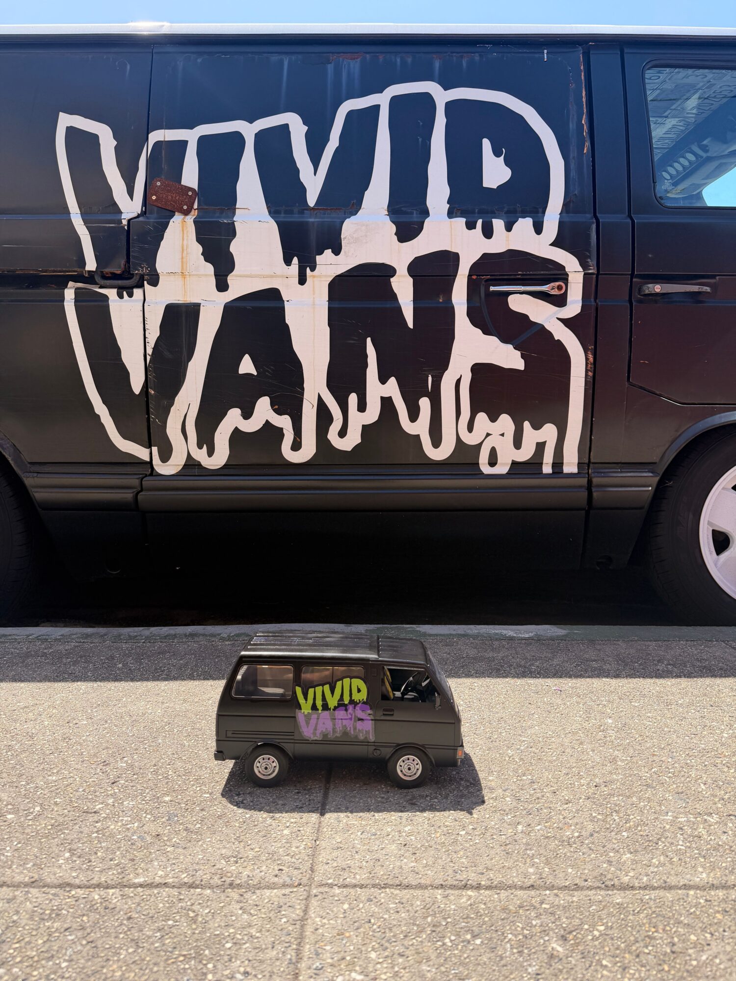Black vehicle with white graffiti-style text on the side, parked on a concrete surface, with a small black object nearby.