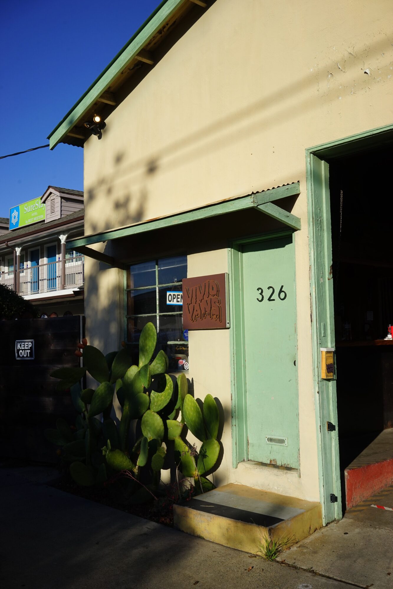 Building entrance with plants, door, and address number 326, under a green awning, against a clear blue sky.