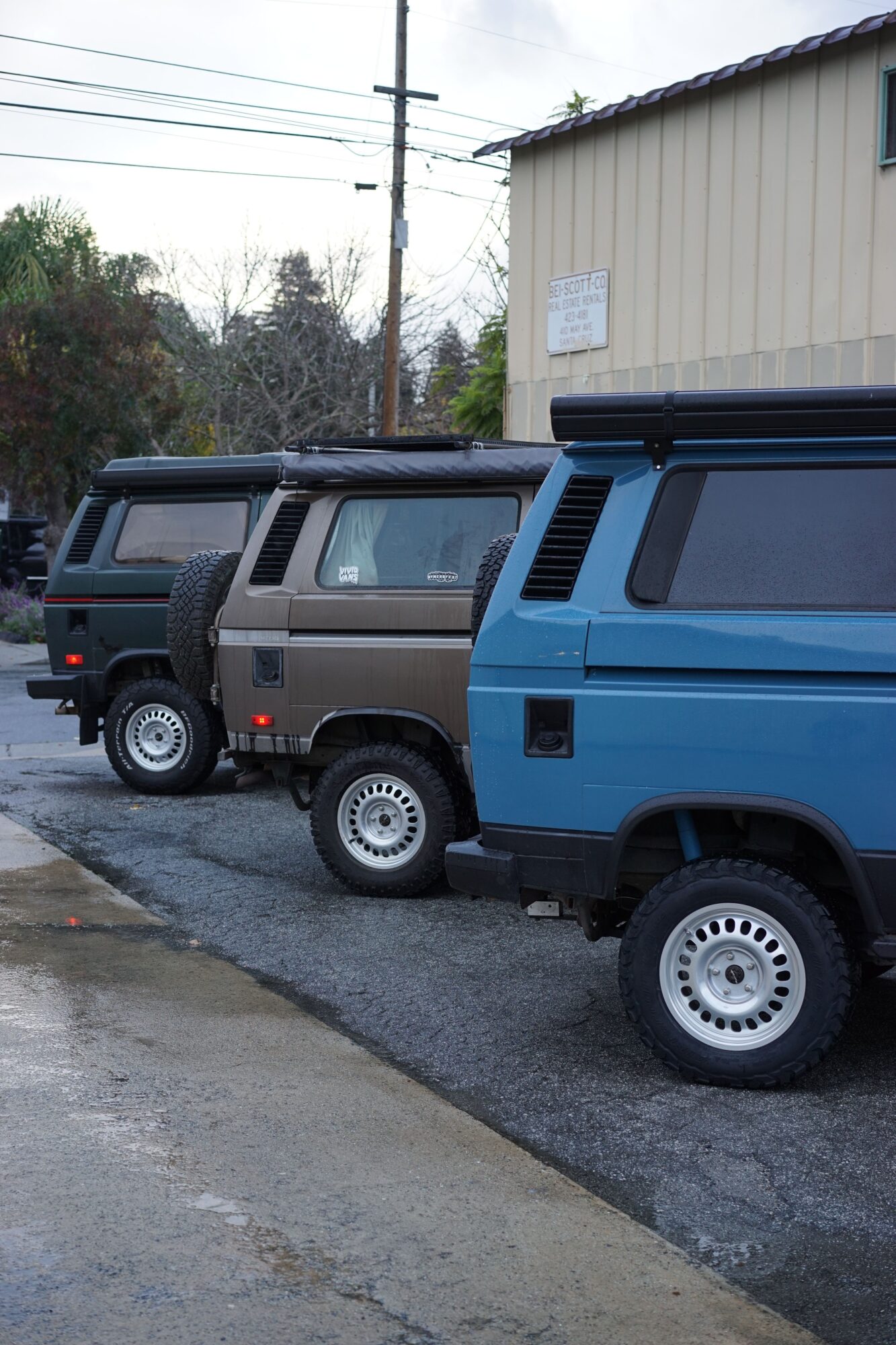 Two vehicles parked on a street, one blue and one black, with a building and power lines in the background.