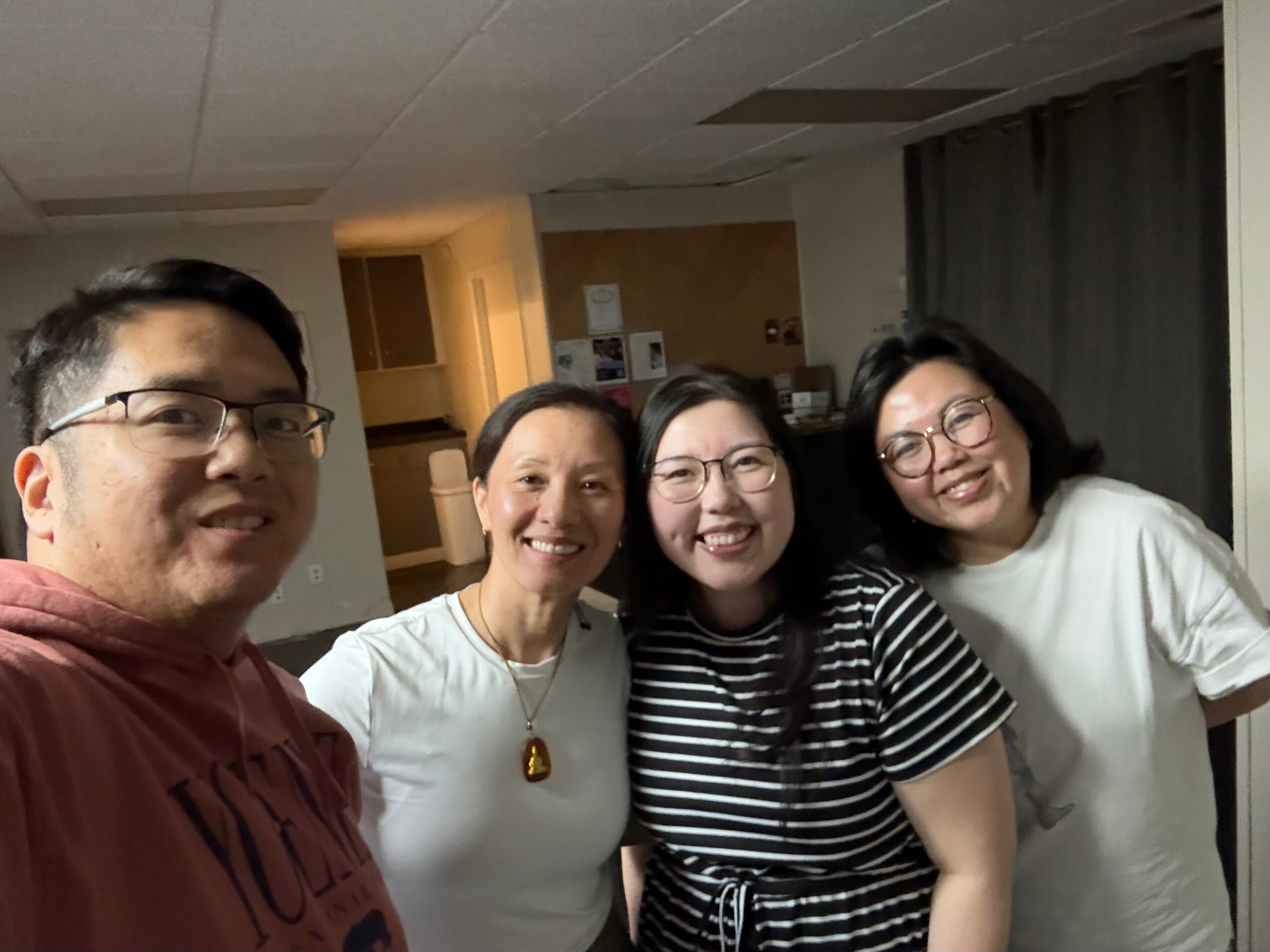 Four people smiling and posing for a photo indoors, with a kitchen area in the background.