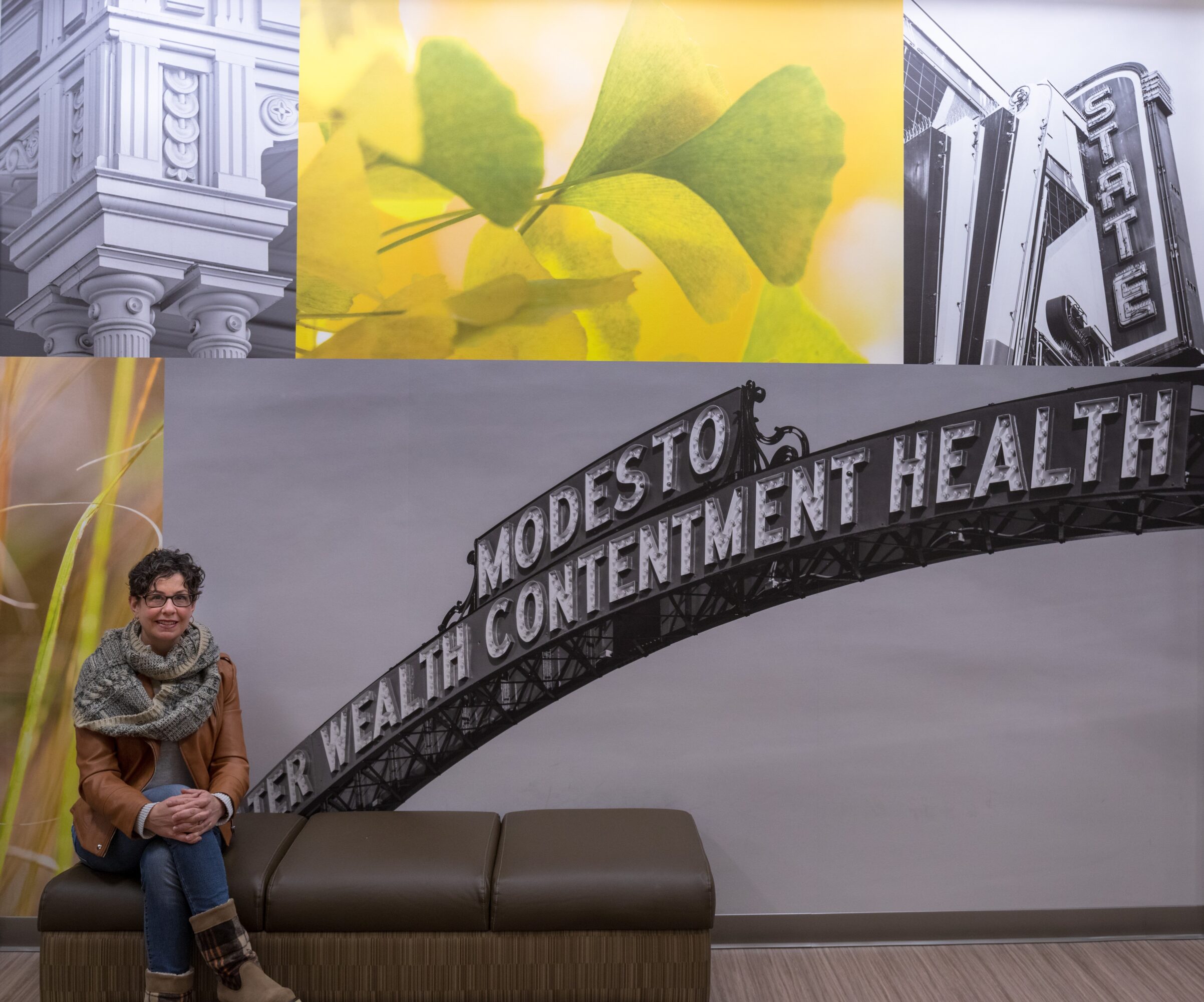 Person sitting on a bench in front of a wall with a sign reading 'Modesto' and 'Health' at a health facility.