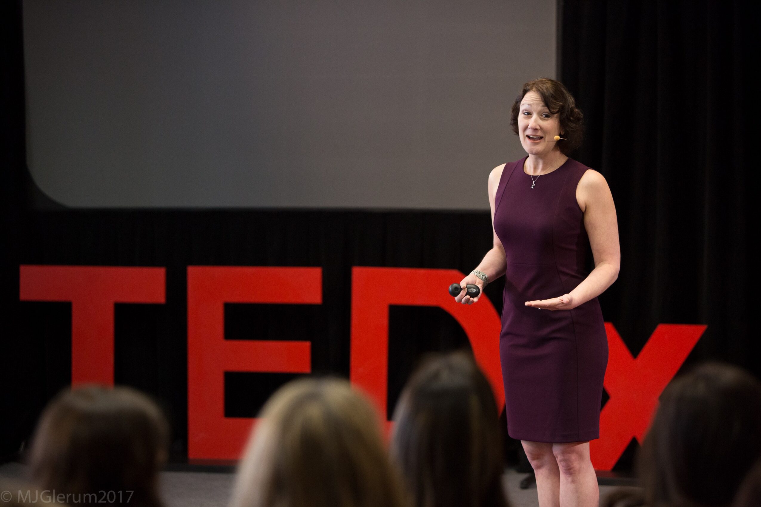 Woman in purple dress speaking on stage with large red TED letters behind her, audience in foreground