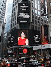 Tall buildings with digital billboards, including a woman in a red top on a large screen, busy city street scene.