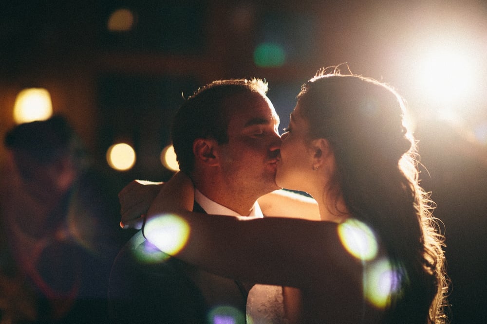 A couple is kissing in a dimly lit setting with bright backlight and bokeh effects.