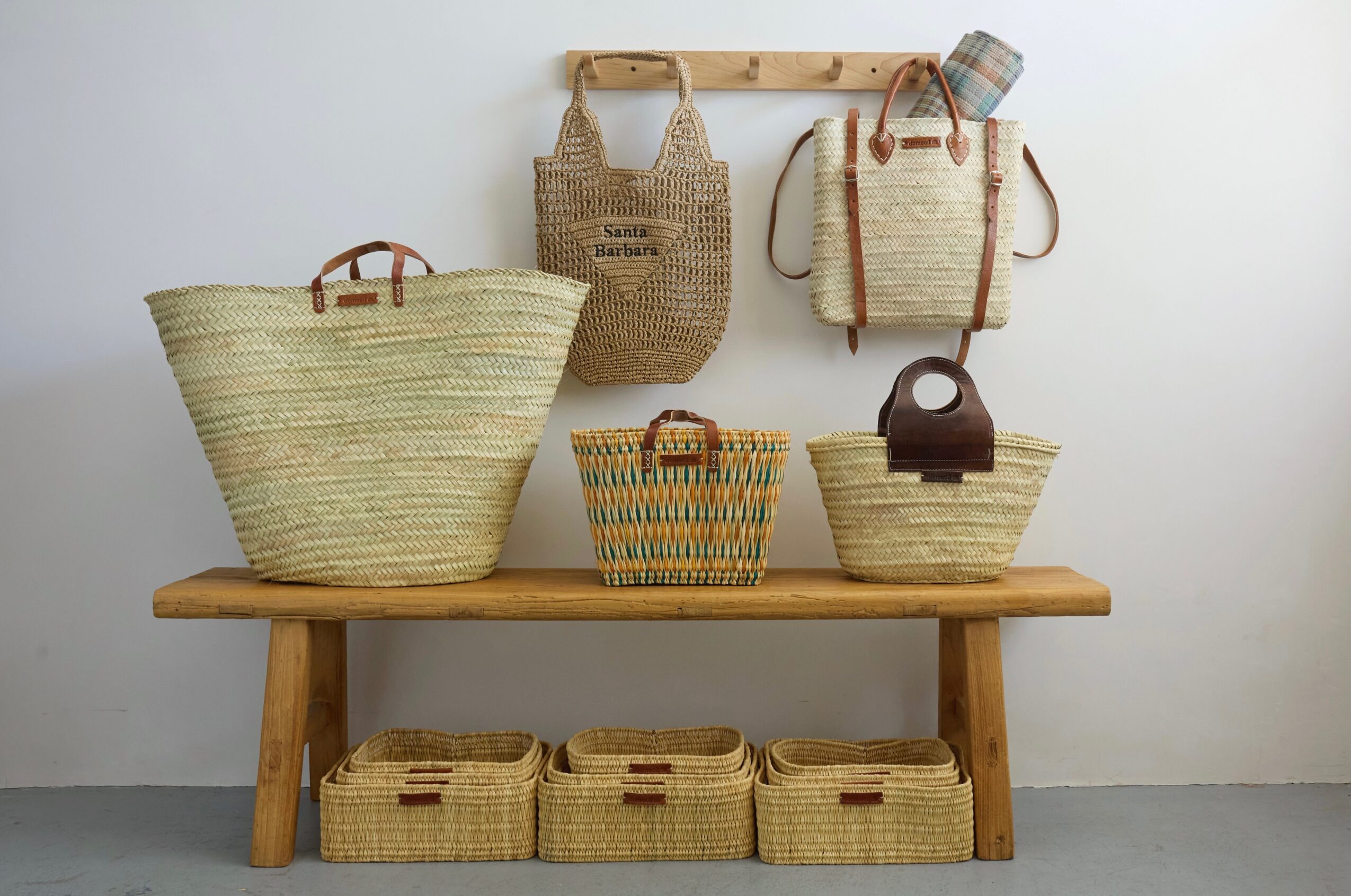 Wooden bench with woven baskets and bags hanging on wall, against plain white background.