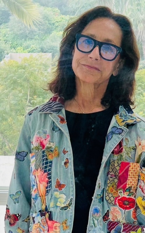 Woman with dark hair and glasses outdoors, wearing a colorful embroidered jacket and black top.