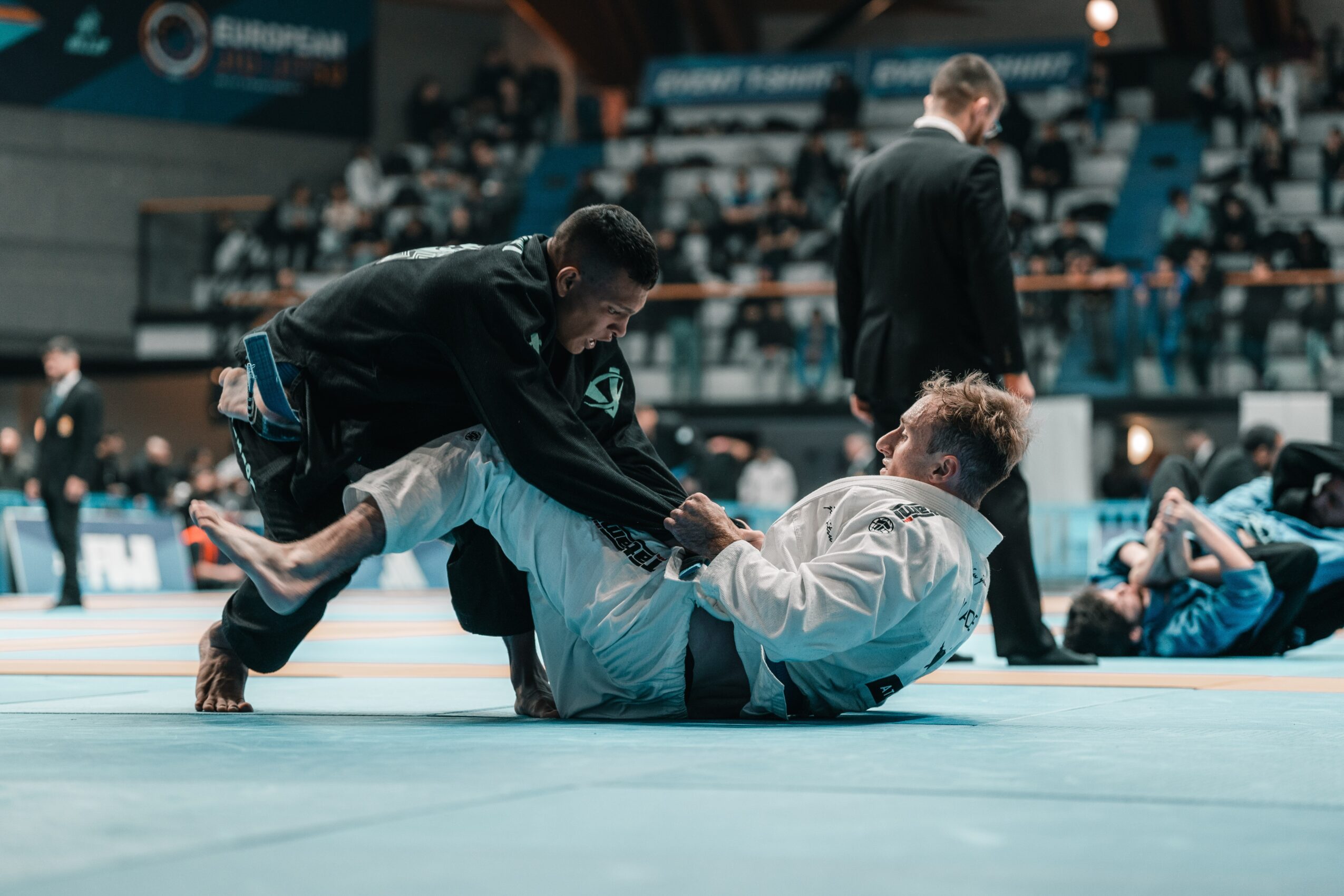 Two judo competitors on the mat, one in a black gi and the other in a white gi, during a match.