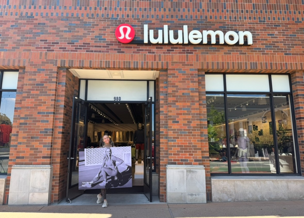 Lululemon store entrance with a person standing outside, brick building, large windows, and logo above door.