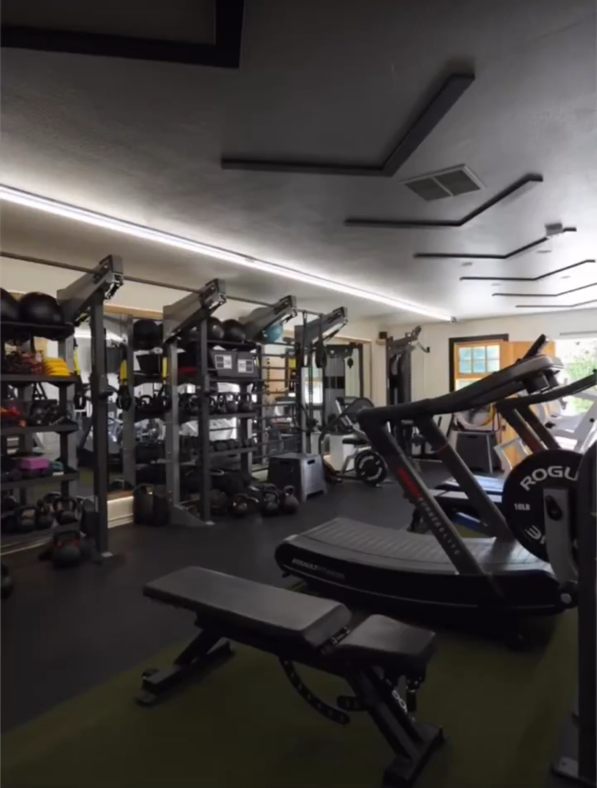 Gym with exercise equipment, including a treadmill and weight racks, in a well-lit room with large windows.