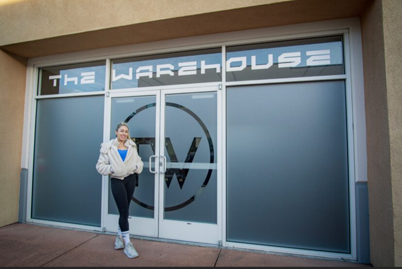 Person standing in front of a large glass door with a logo and text reading 'The Warehouse'.
