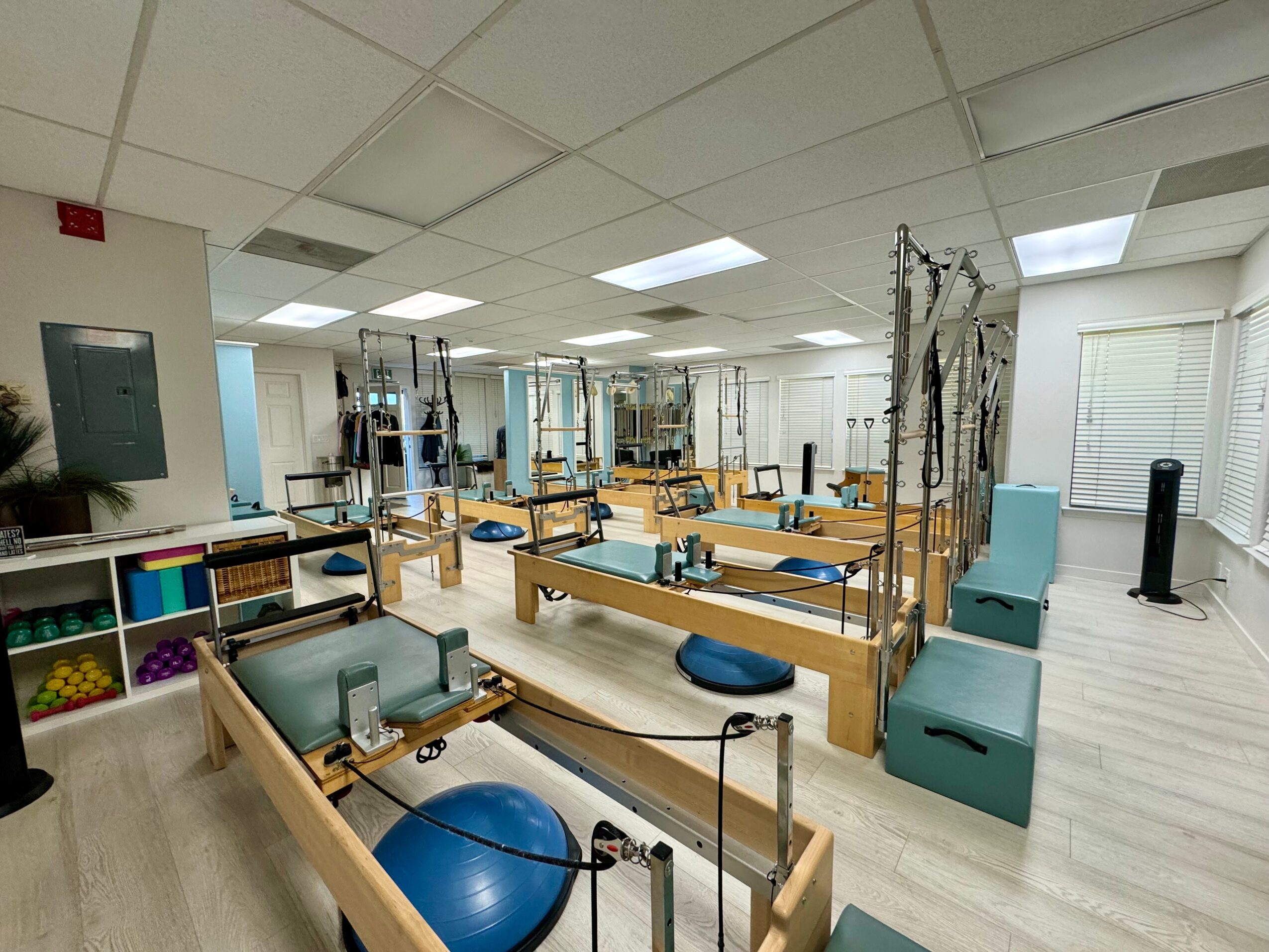 Physical therapy room with tables, equipment, and exercise balls, well-lit with ceiling lights and windows, organized for therapy sessions.