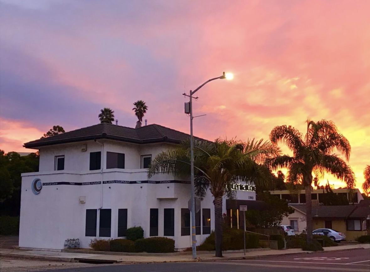 White building with palm trees and a streetlamp against a colorful sunset sky.