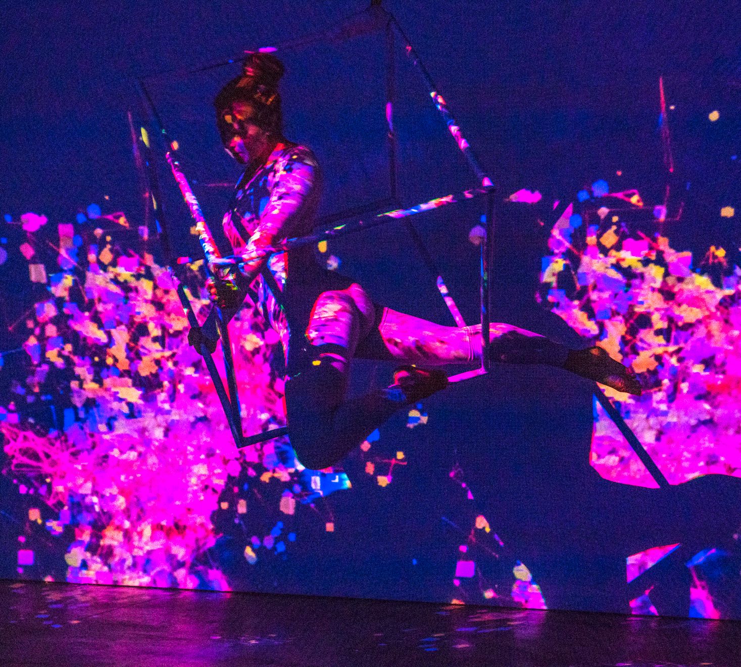 Person on a swing with colorful splashes in the background, illuminated by purple and pink lights.