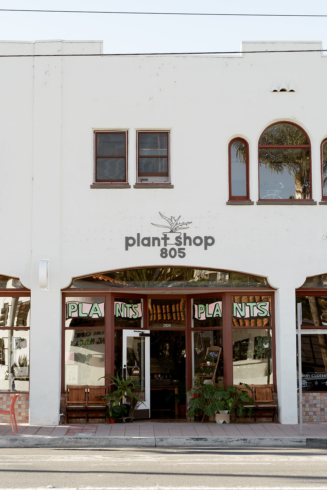 White building with two small windows and an arched window, storefront with plants, and a sign reading 'plant shop 805'.
