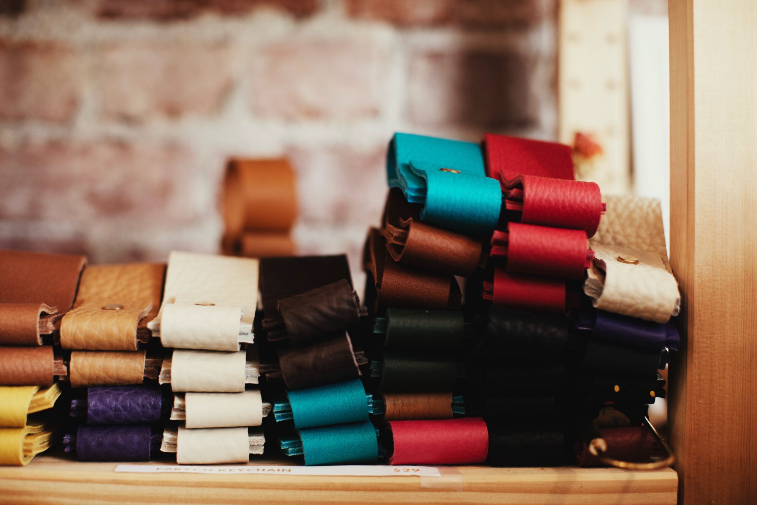 Stacks of colorful fabric rolls arranged on a shelf against a brick wall background.