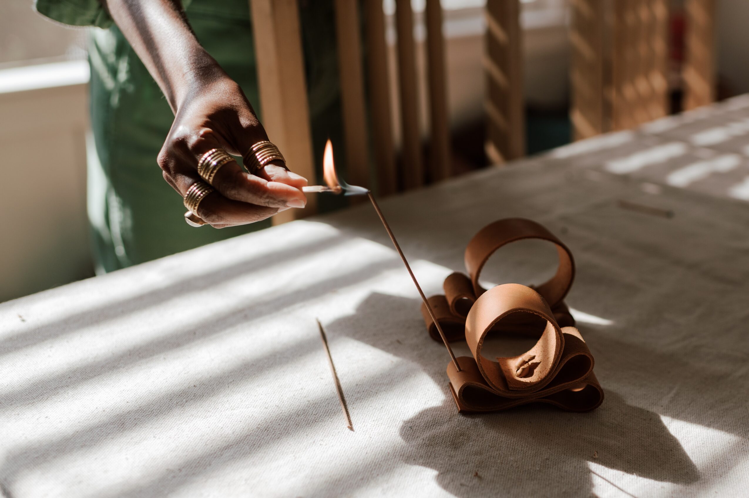 Person lighting a candle with a match, with curled paper on a table, sunlight casting shadows.