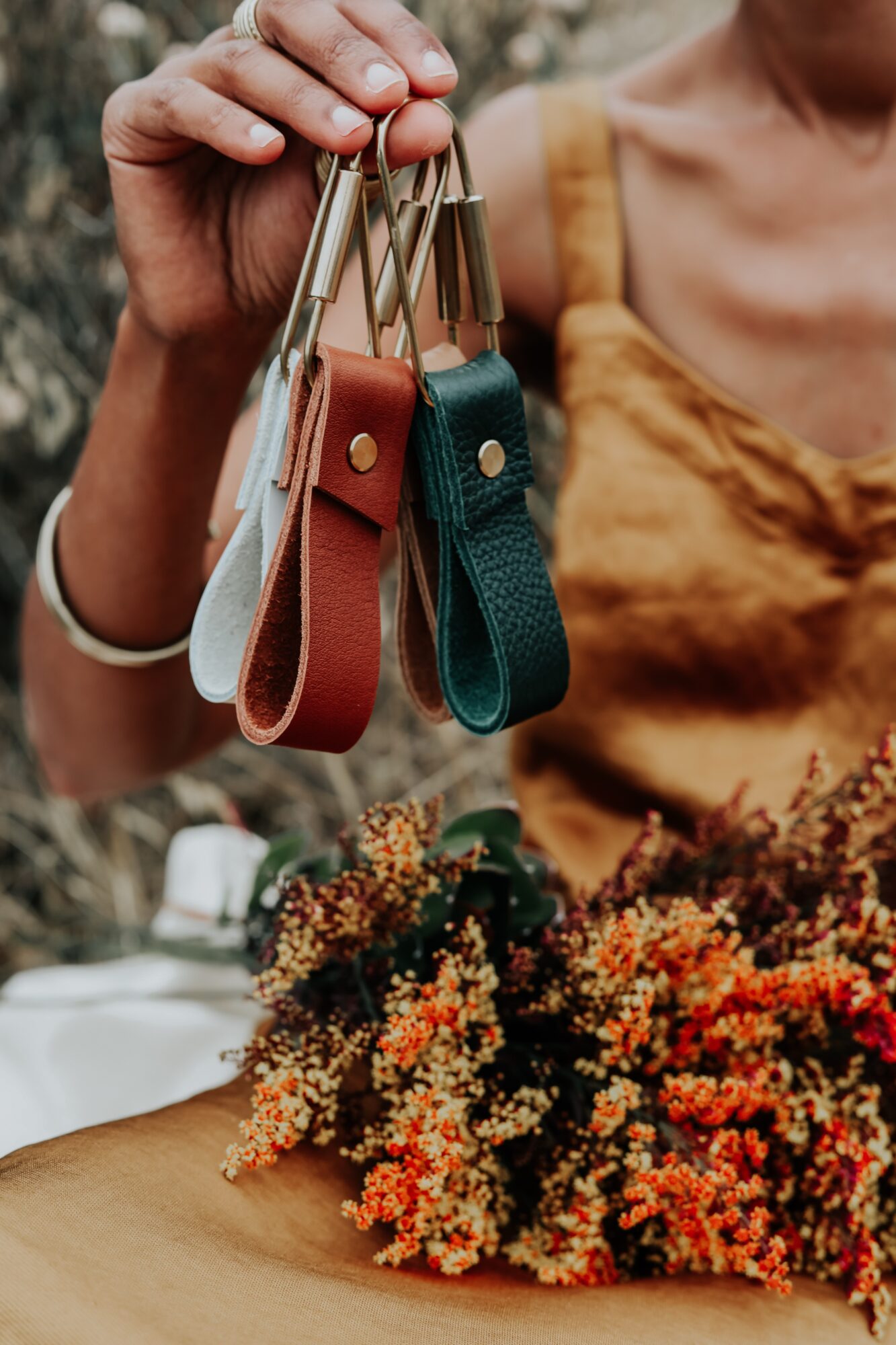 Person holding colorful keychains with a bouquet of orange and red flowers nearby.