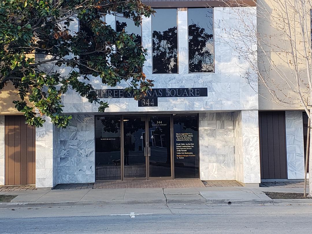 Building with glass doors and windows, street view, trees reflected in windows, street sidewalk in front.