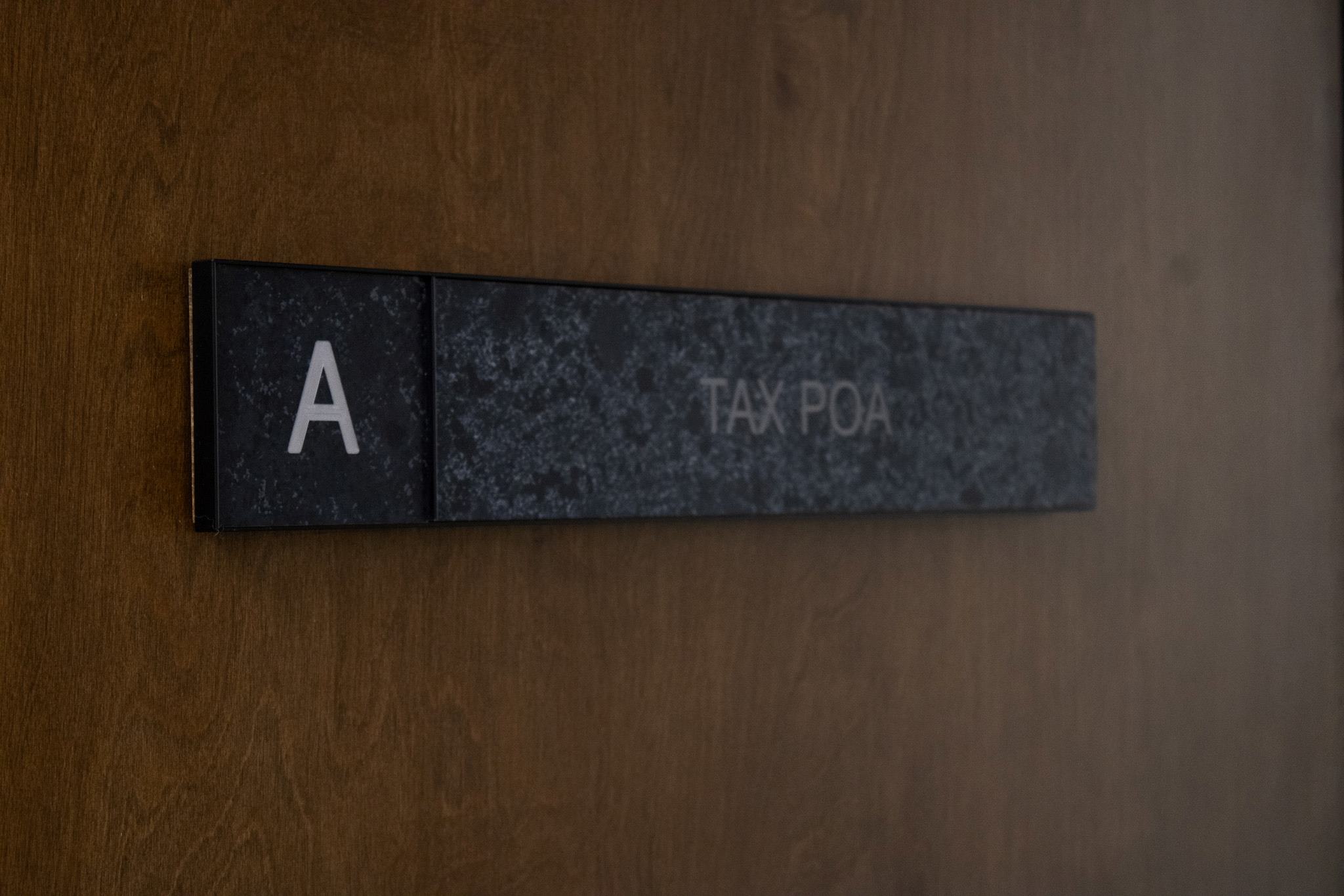 Black rectangular sign with a white letter 'A' on the left and the words 'TAX POA' on the right, mounted on a wooden surface.