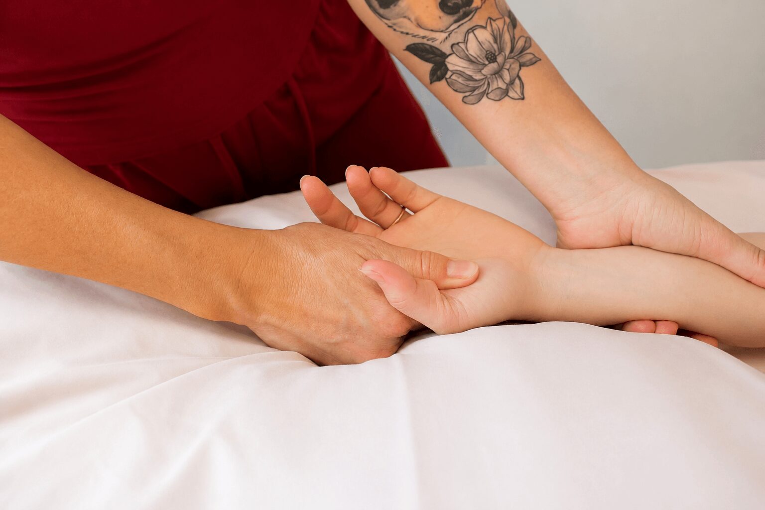 Person receiving a hand massage, with a tattooed arm, on a white surface.