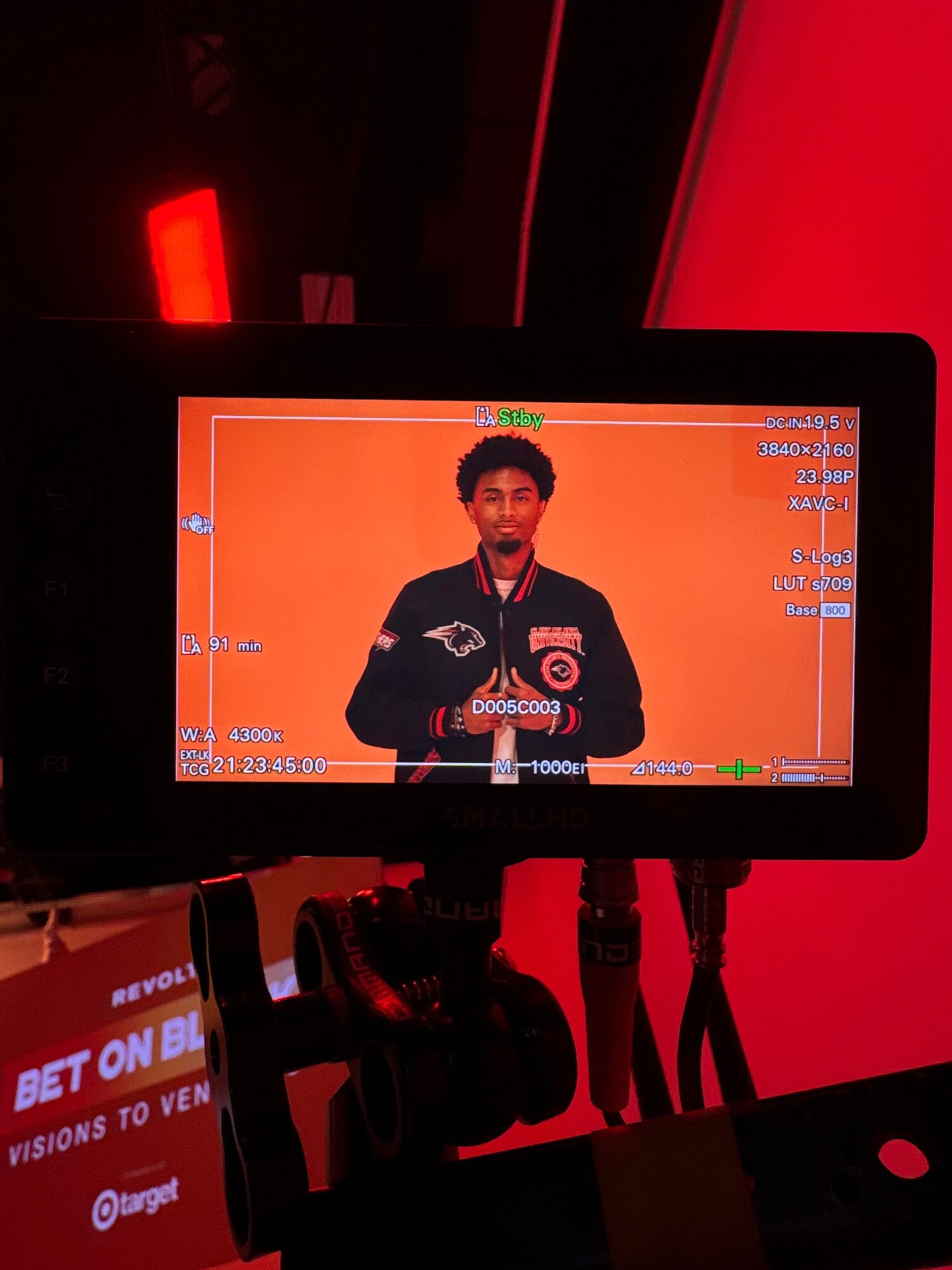 Screen displaying a person in a black jacket with text, against an orange background, with gaming interface elements visible.