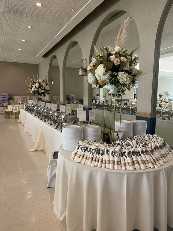 Elegant banquet table with floral centerpieces and desserts in a spacious, well-lit room with arched windows.