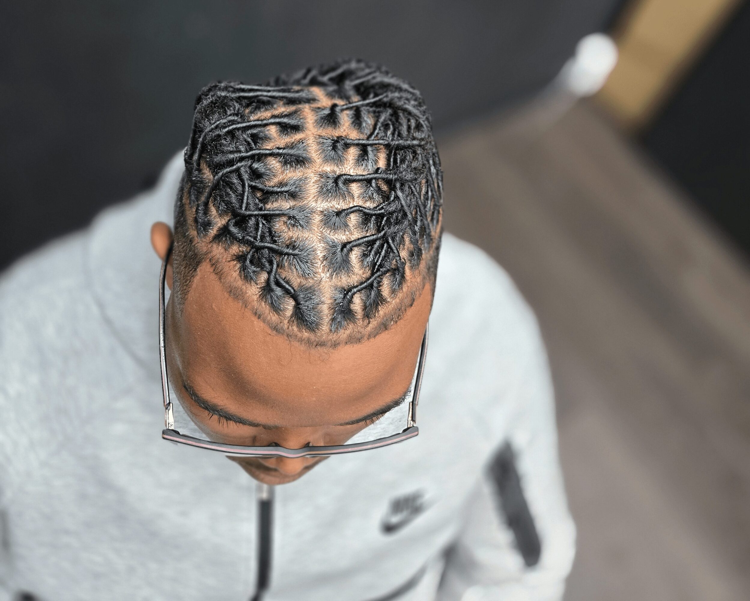 Top view of a person with neatly styled dreadlocks and glasses, wearing a light gray hoodie.