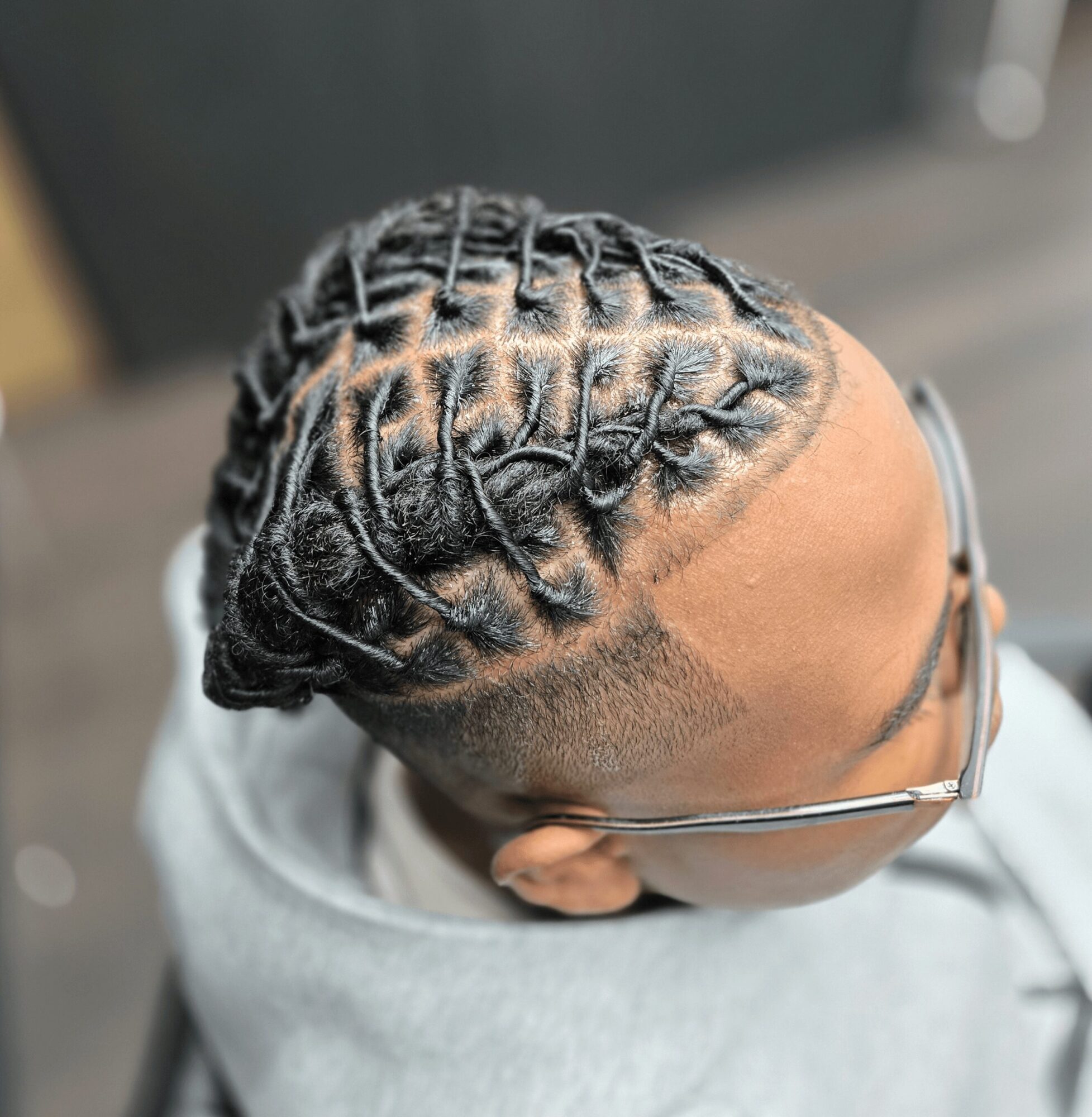 Top view of a person with intricately styled braided hair and glasses, wearing a light-colored hoodie.