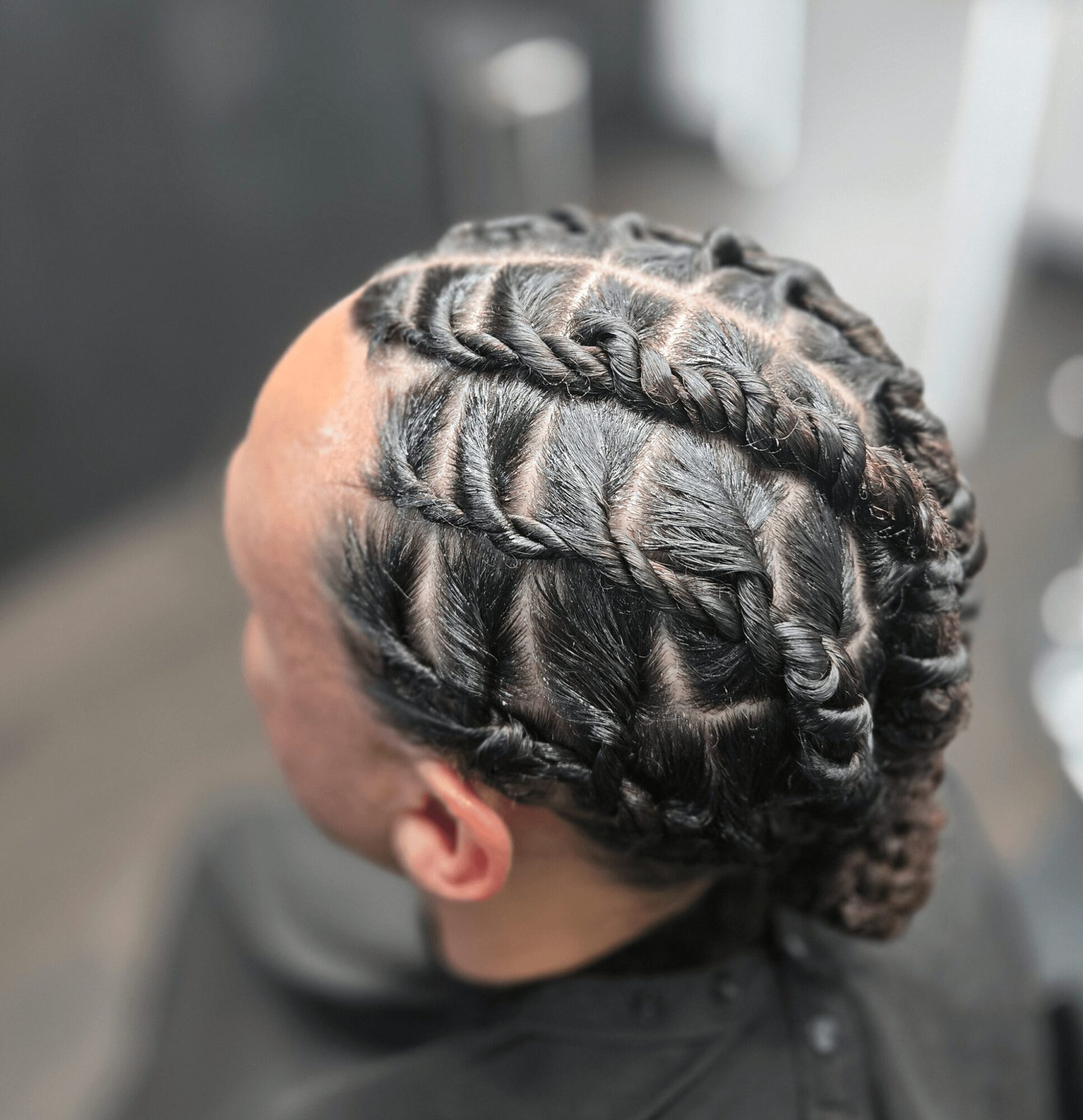 Person with braided hairstyle viewed from above, showing multiple thick braids arranged in a pattern on the scalp.