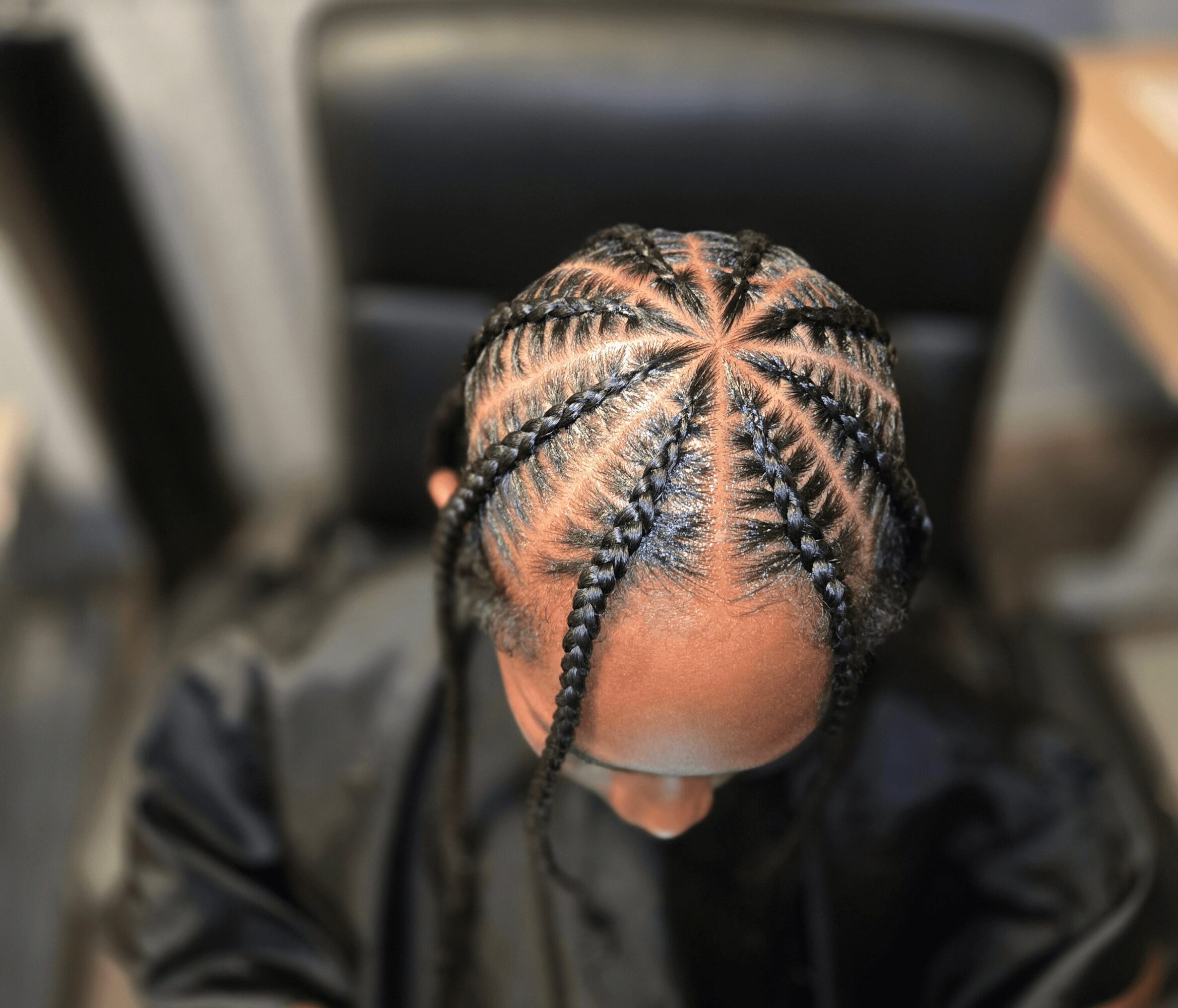 Top view of a person with braided hair styled in a star pattern, head tilted downward, indoors.