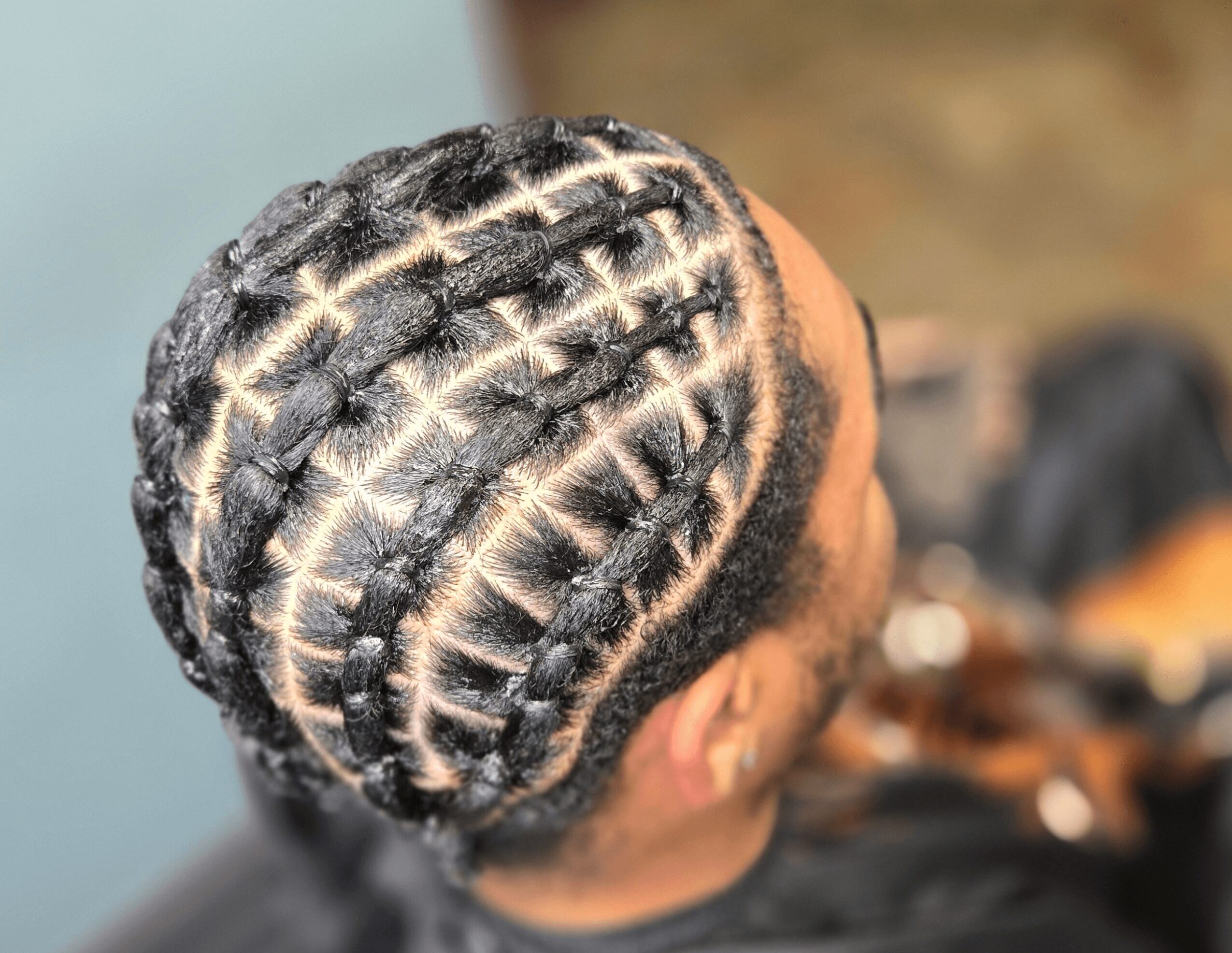 Close-up of a person's head with neatly braided hair styled in cornrows, viewed from above.
