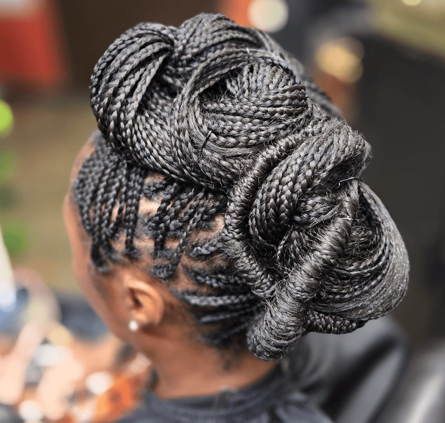 Back view of a person with intricately styled braided hair arranged in an updo, with a large decorative bun on top.