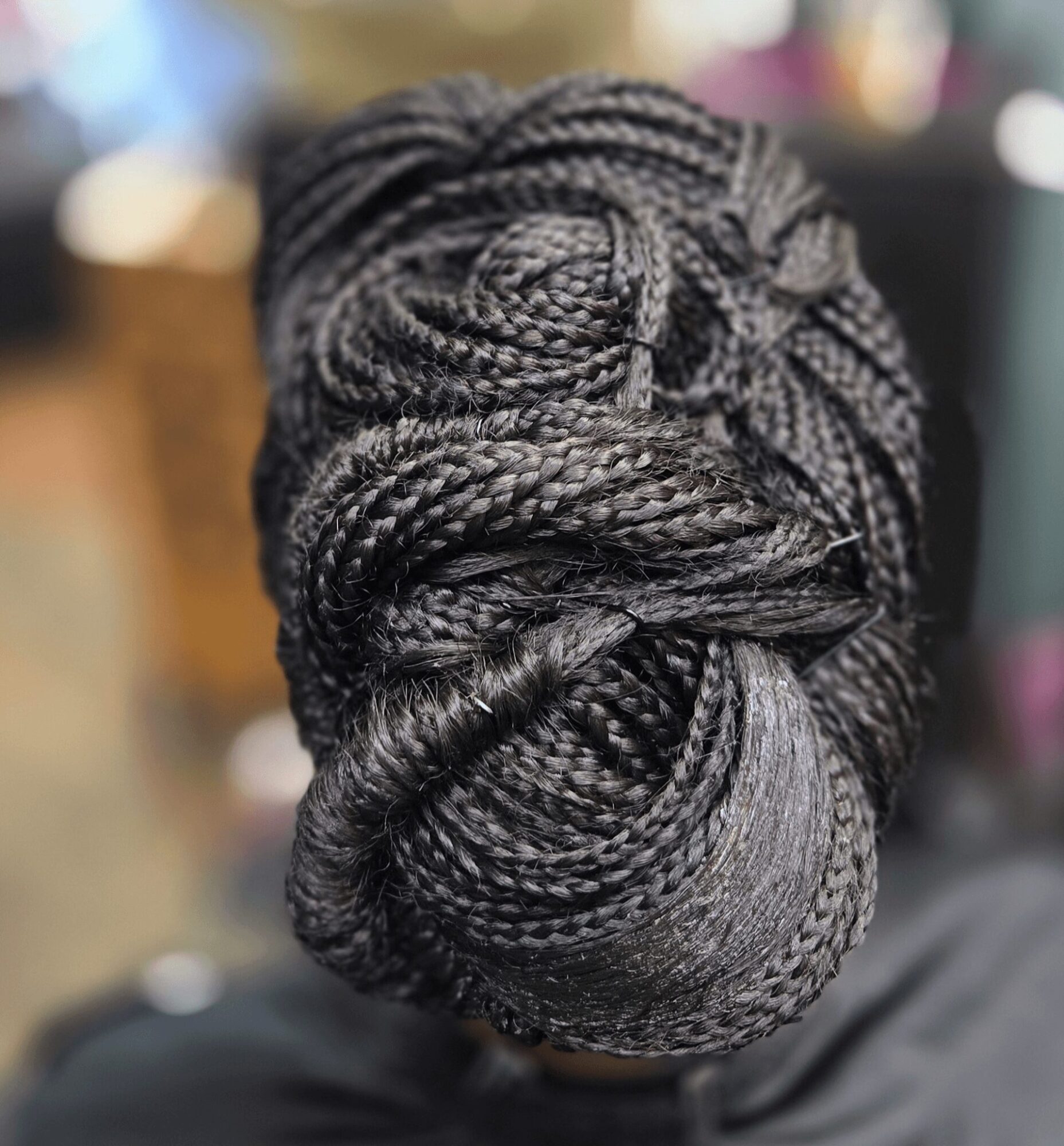 Close-up of intricately styled braided hair in a bun, with a blurred background.