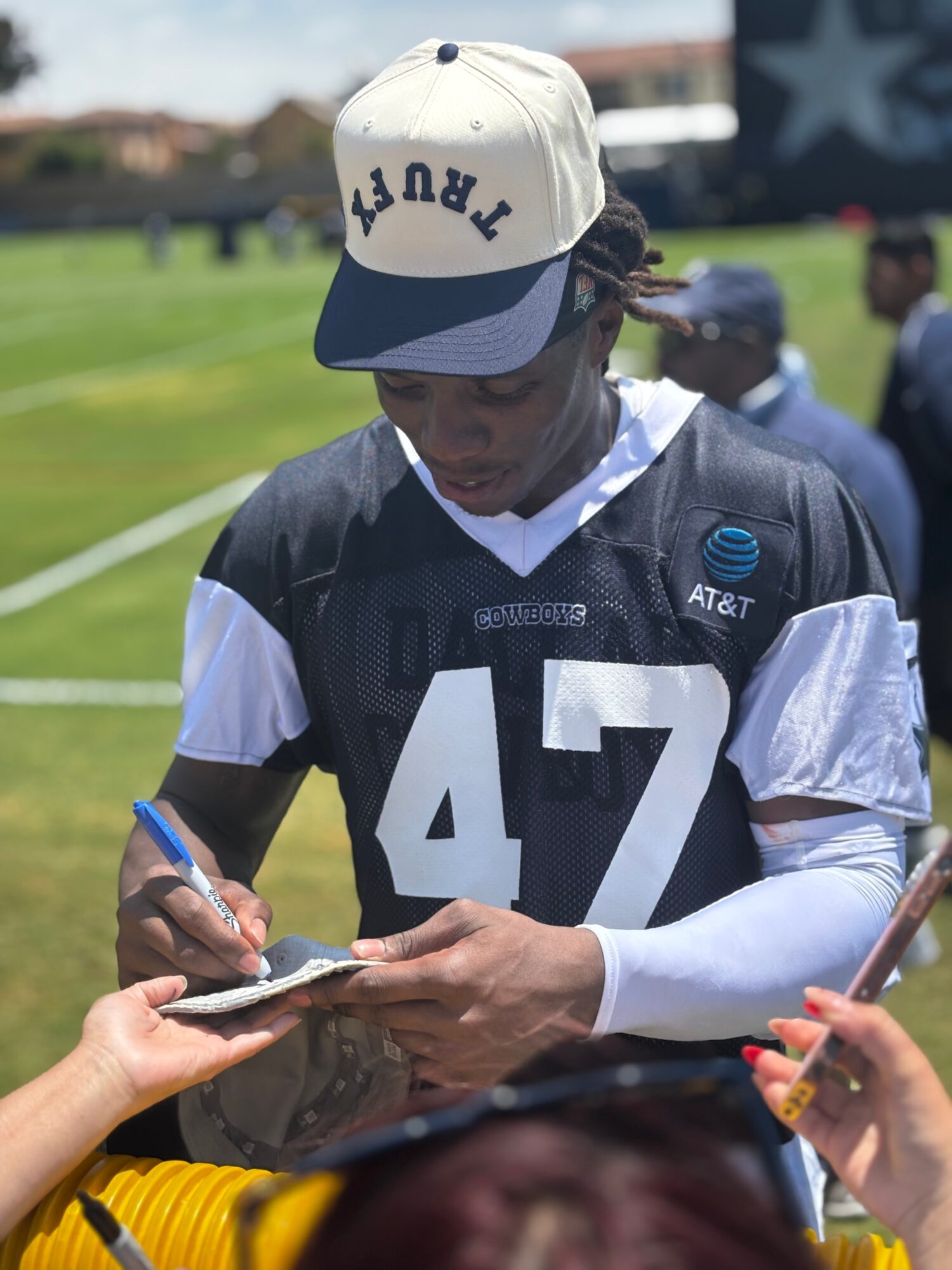 Person in football uniform signing autographs on a football field, wearing a cap and jersey number 47.