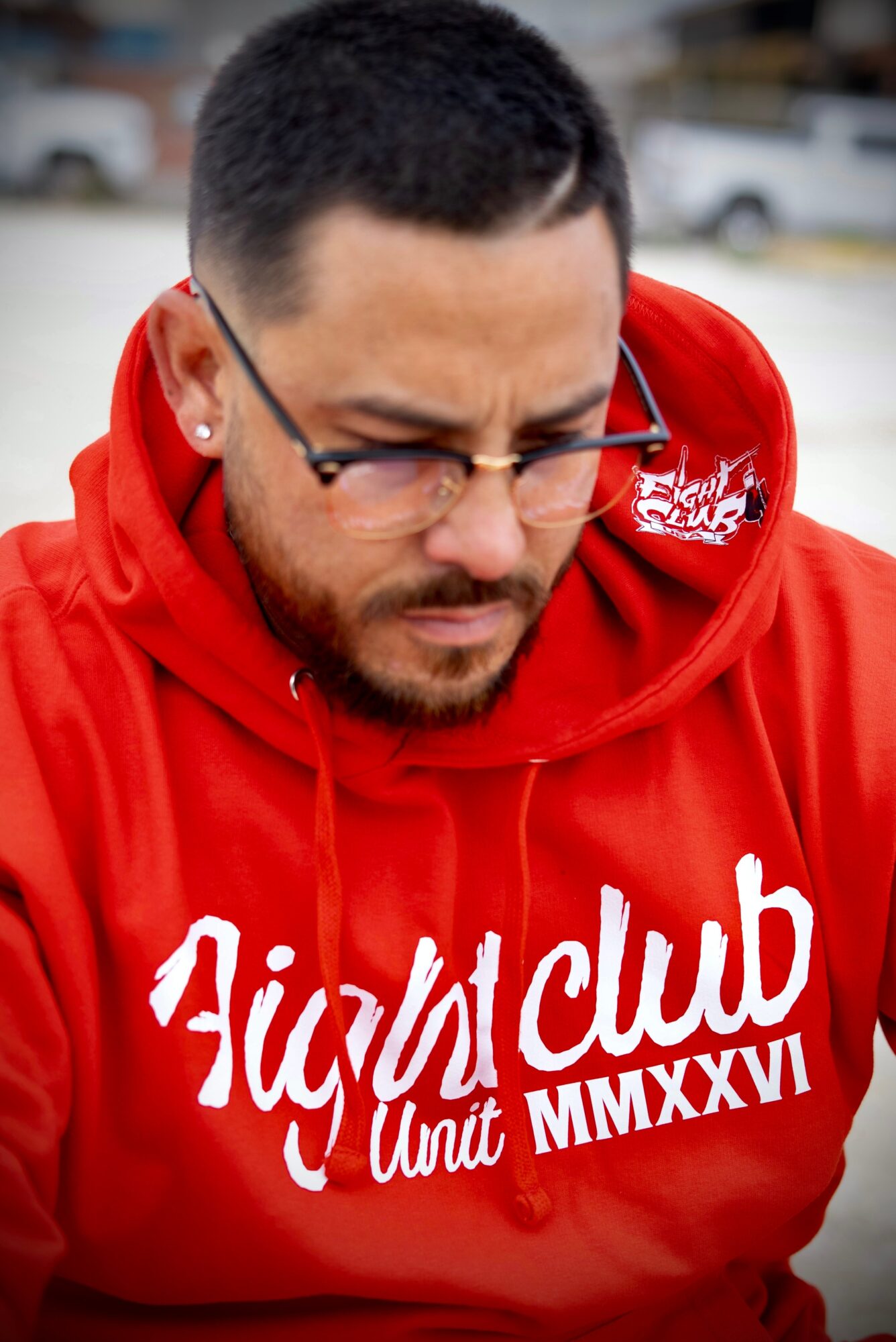 Man with glasses and a beard wearing a red hoodie with white text, looking downward.