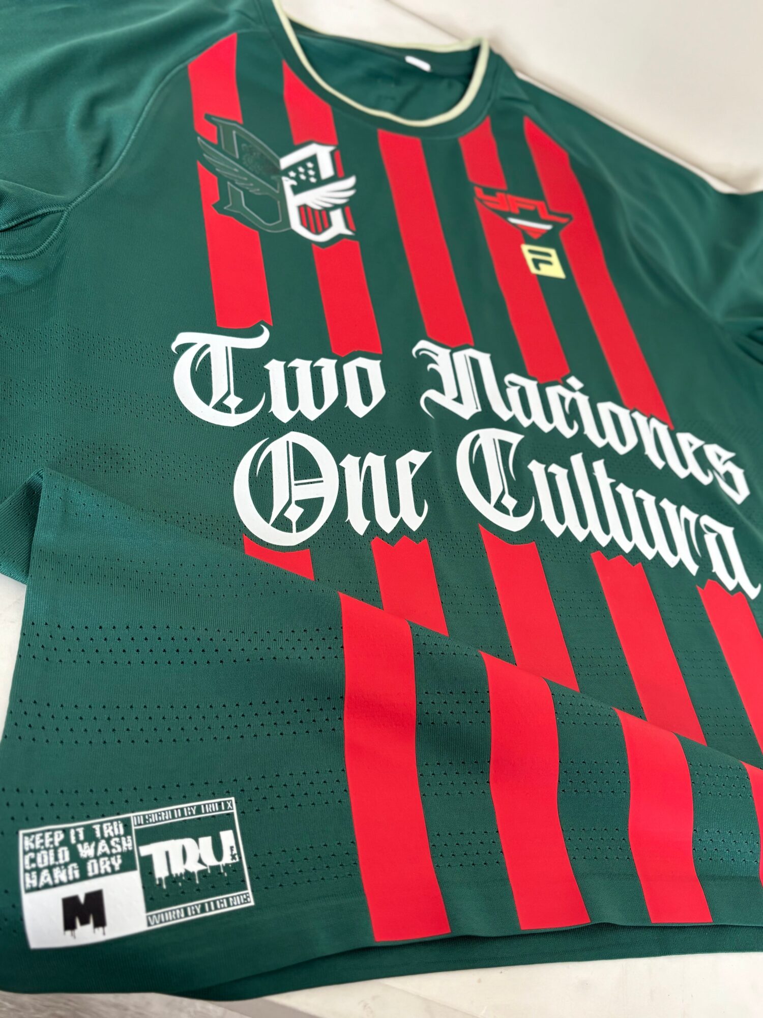 Green sports jersey with red and black vertical stripes, white text, and logos, laid flat on a surface.