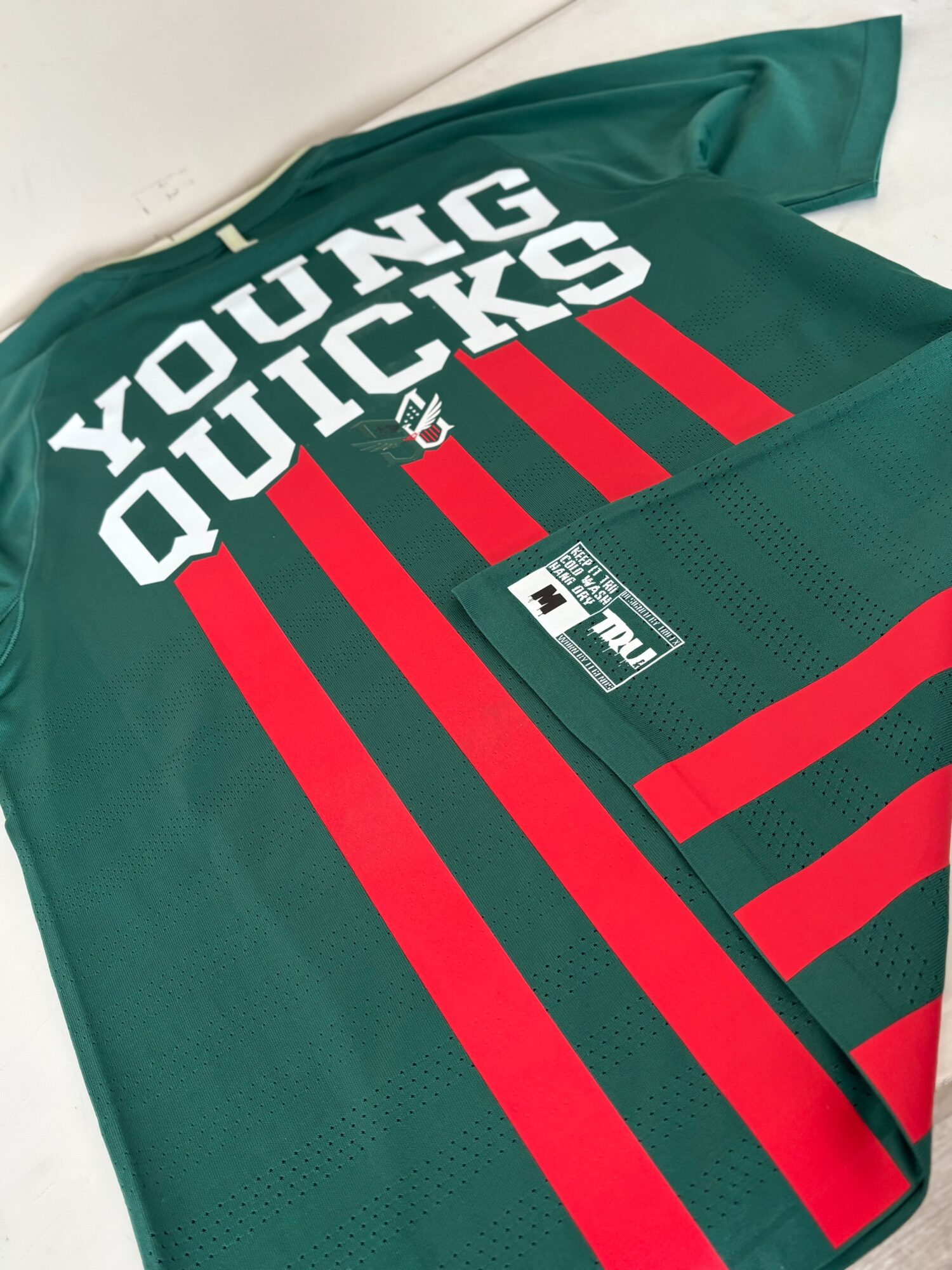 Green sports jersey with white text and red stripes, partially folded, on a white surface.