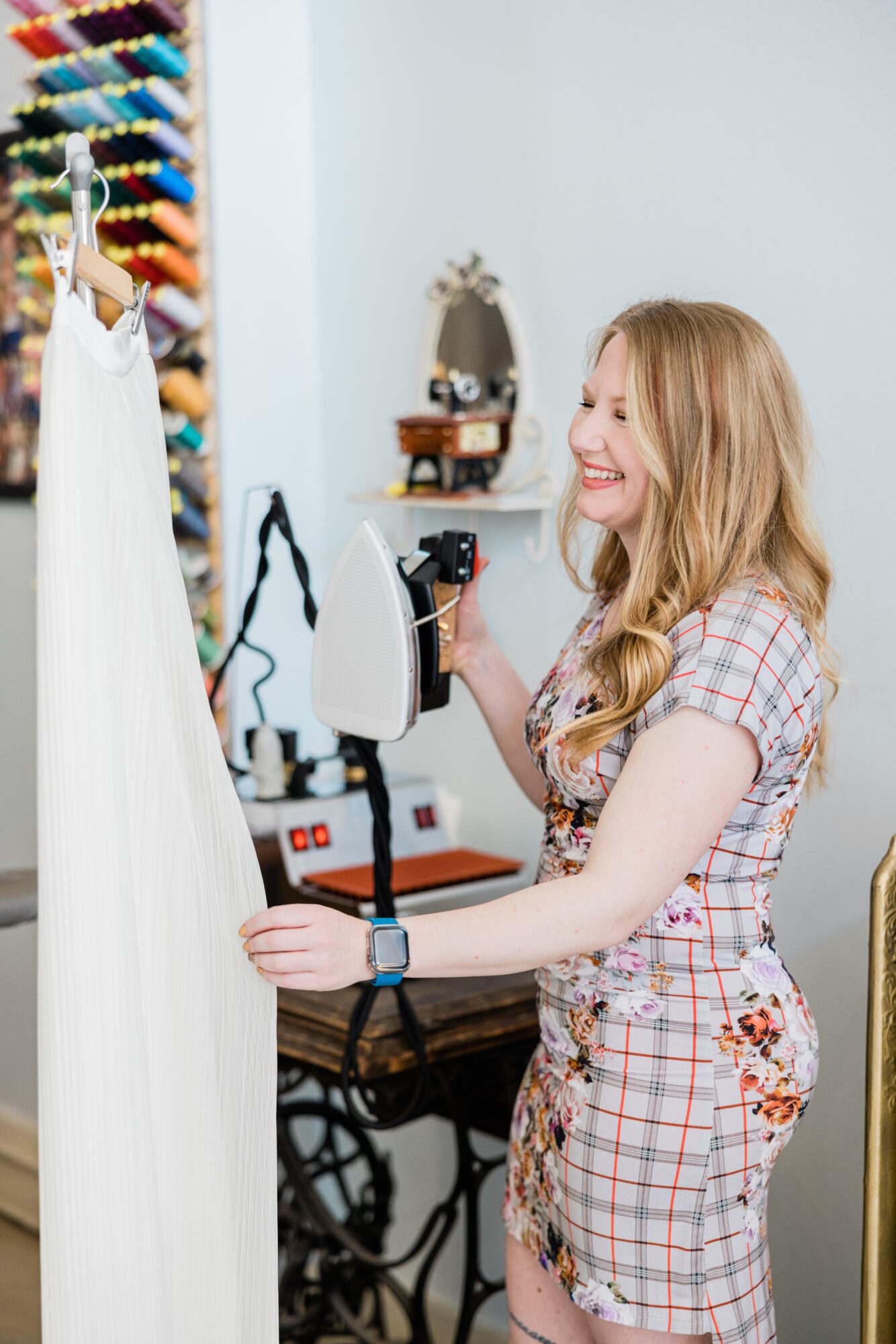 Young woman smiling while using an iron on a dress in a sewing room.