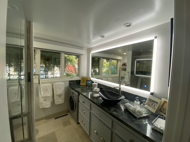Laundry room with windows, countertop, washing machine, and framed photos, illuminated by bright lighting.